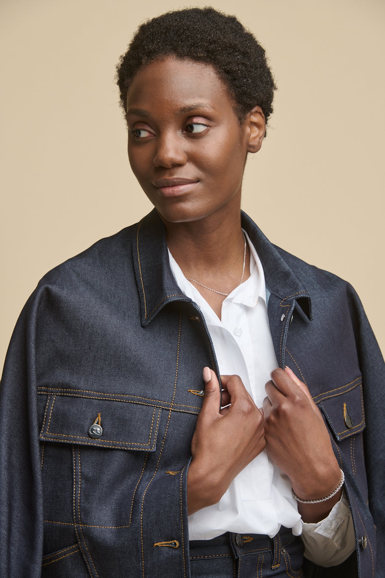 Portrait of female wearing Jodie denim jacket over her shoulders in indigo denim with Olivia shirt in white underneath