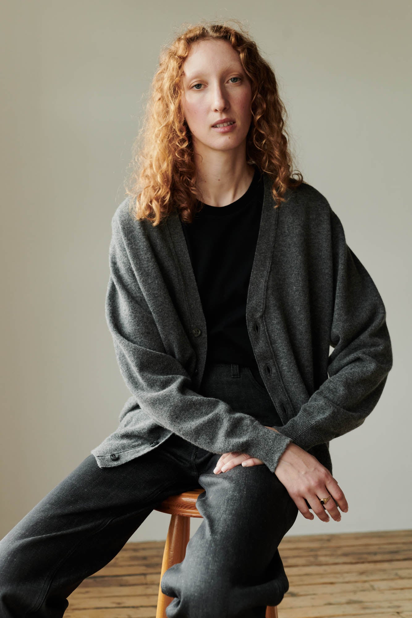 Fair skinned female with ginger hair wearing lambswool v neck cardigan in charcoal paired with black jeans.