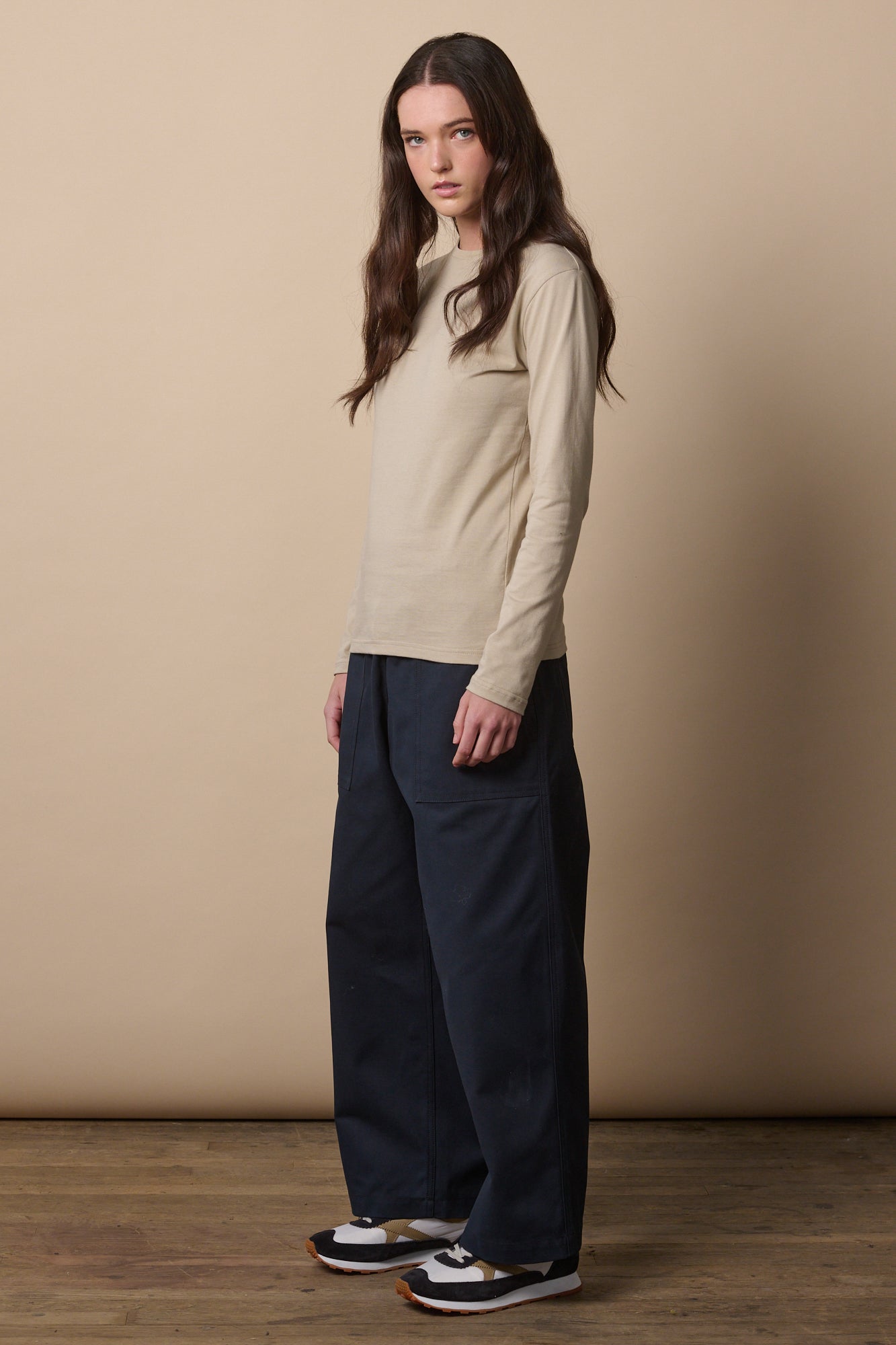 Full body image of brunette female wearing long sleeve t shirt in stone