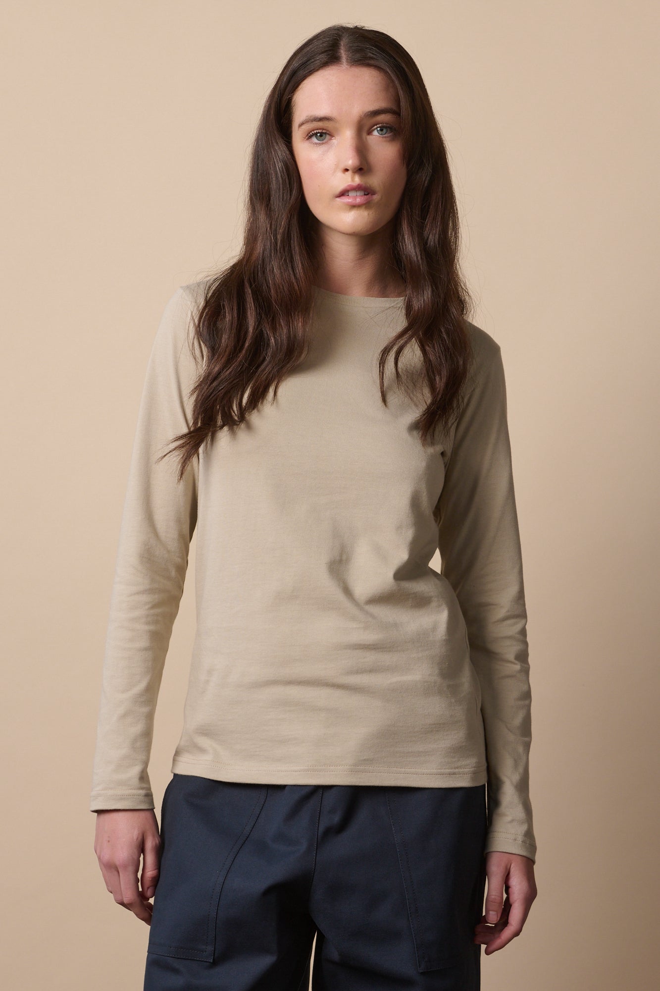 Thigh up image of white female with long brown hair wearing long sleeve t shirt in stone