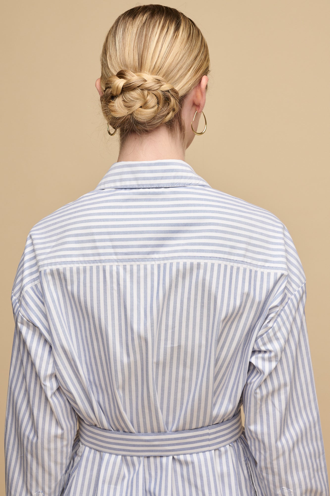 waist up image of the back of white female with blonde hair tied back into low bun wearing belted midi cotton shirt dress in white blue stripes