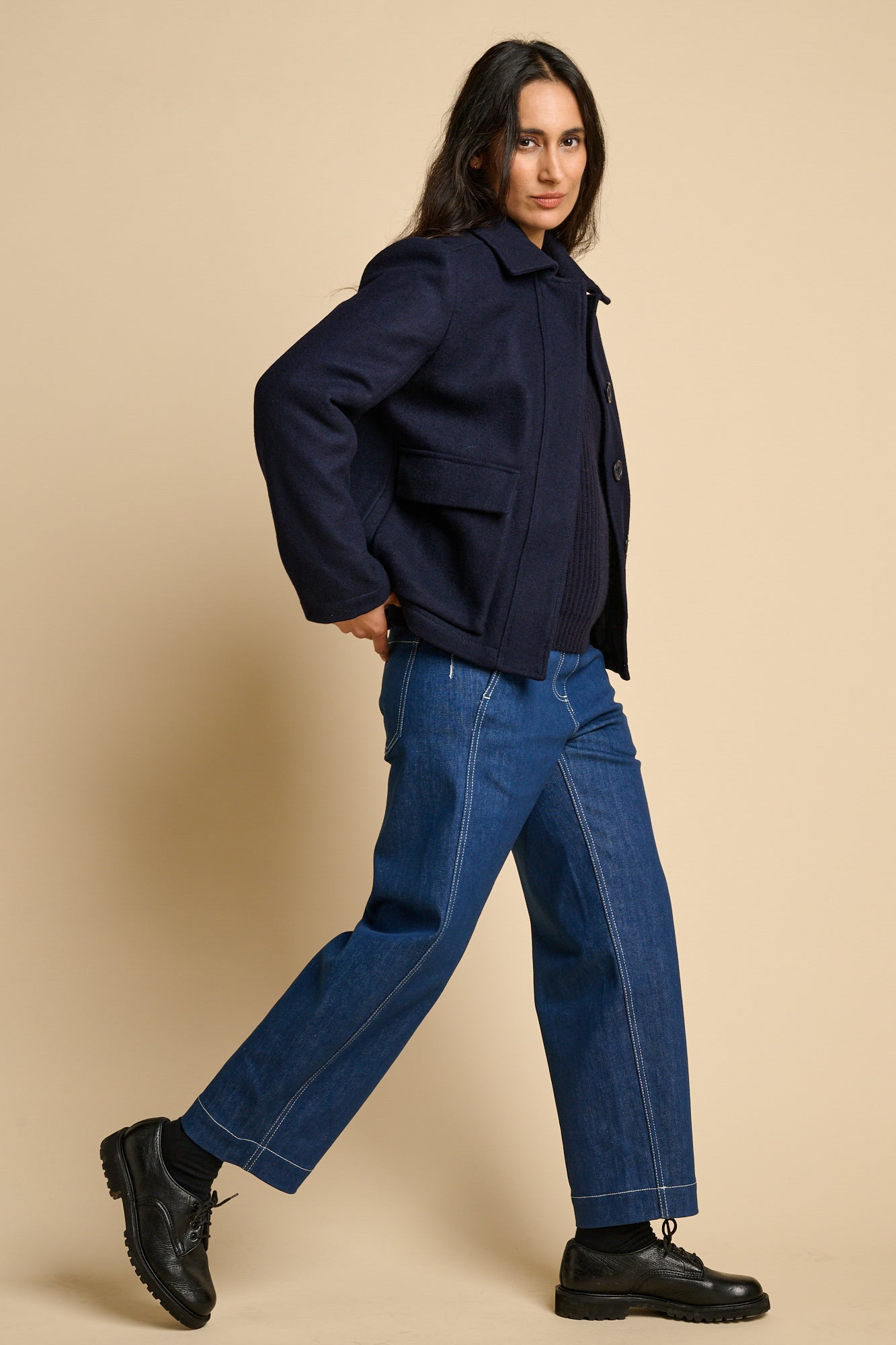 The side of a woman wearing Nancy short wool coat in navy paired with blue jeans and black shoes.