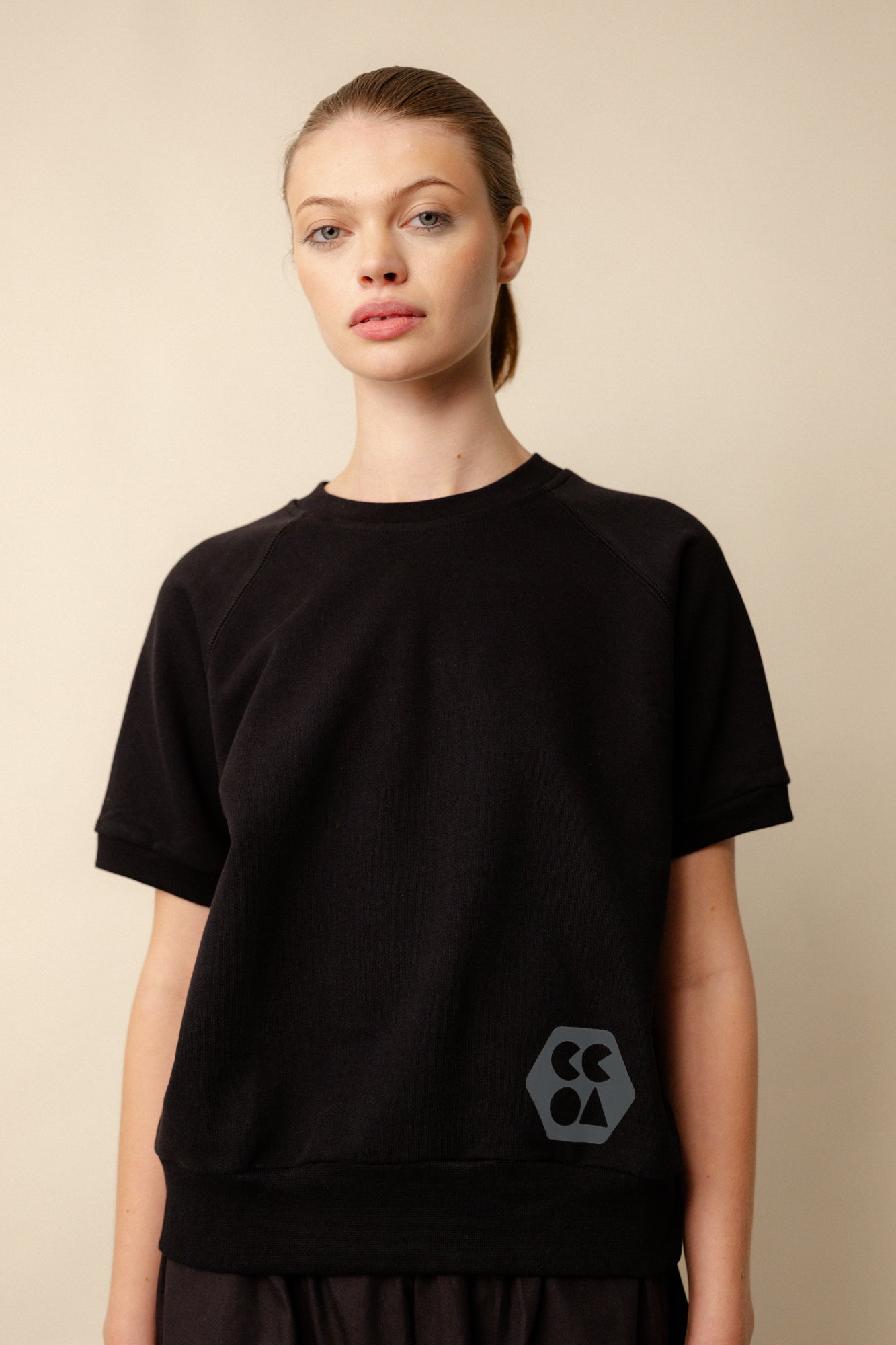 female wearing short sleeve raglan training top plastic free in black with CCOA logo at hem