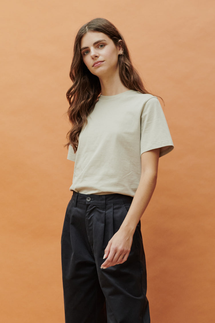 Thigh up front of female wearing short sleeve t shirt in stone paired with pleated trousers in navy