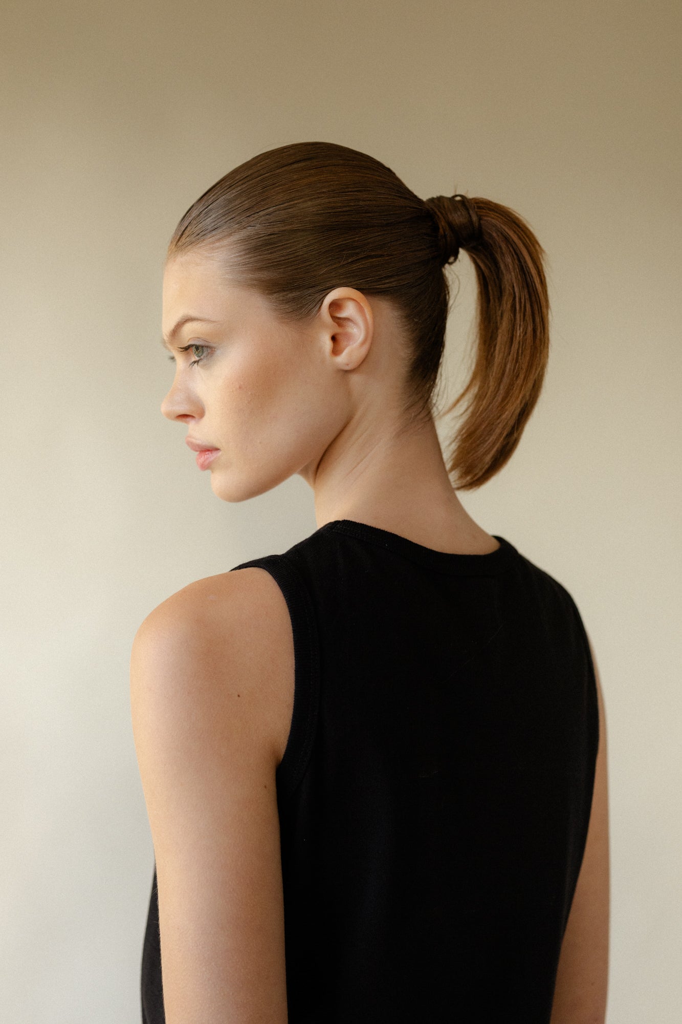 Shot of back of female with hair in ponytail looking to side showing side of face profile, wearing sleeveless t shirt in black