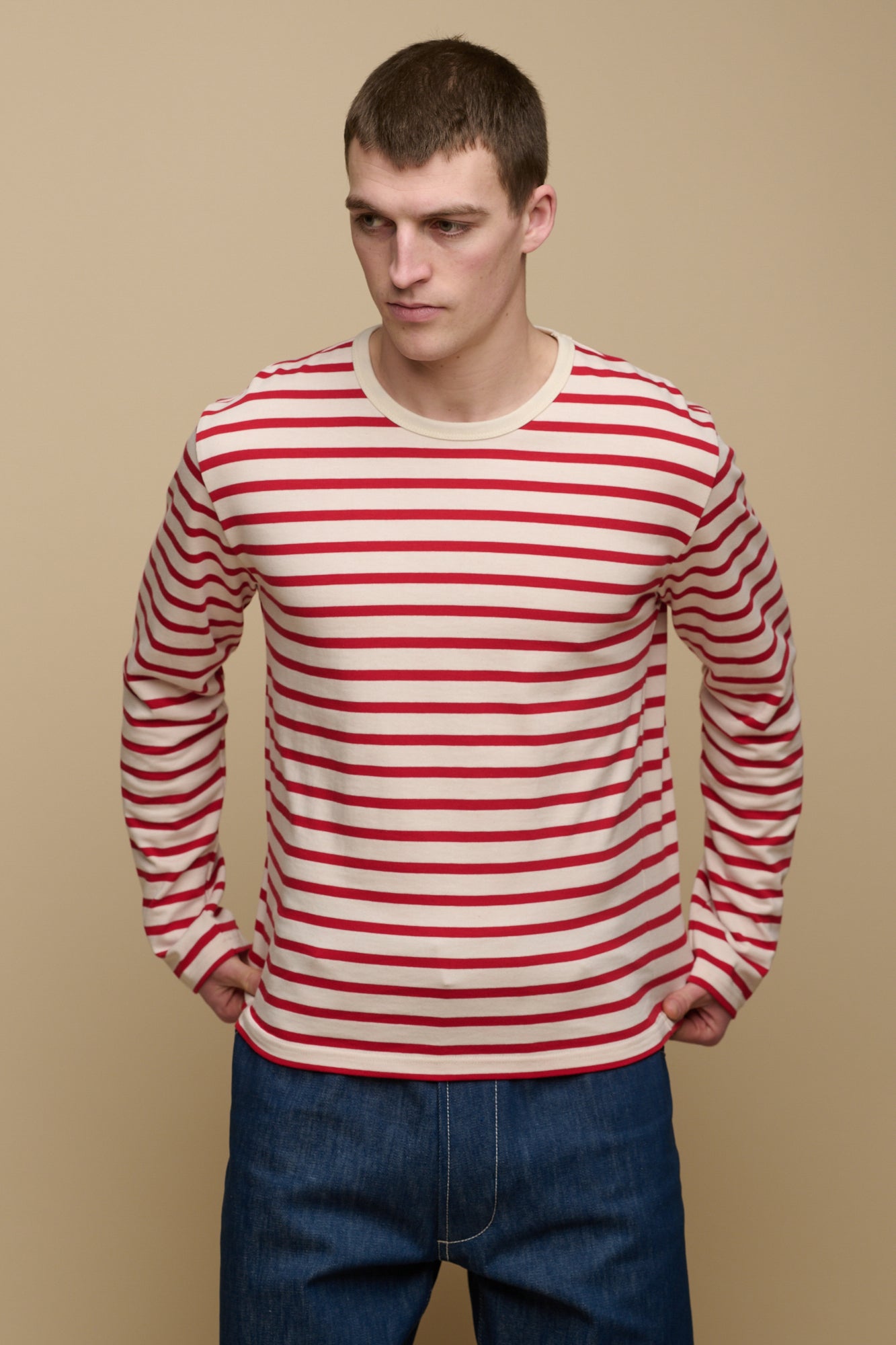 Thigh up image of brunet male wearing ecru/flame red Breton paired with men's jeans in blue