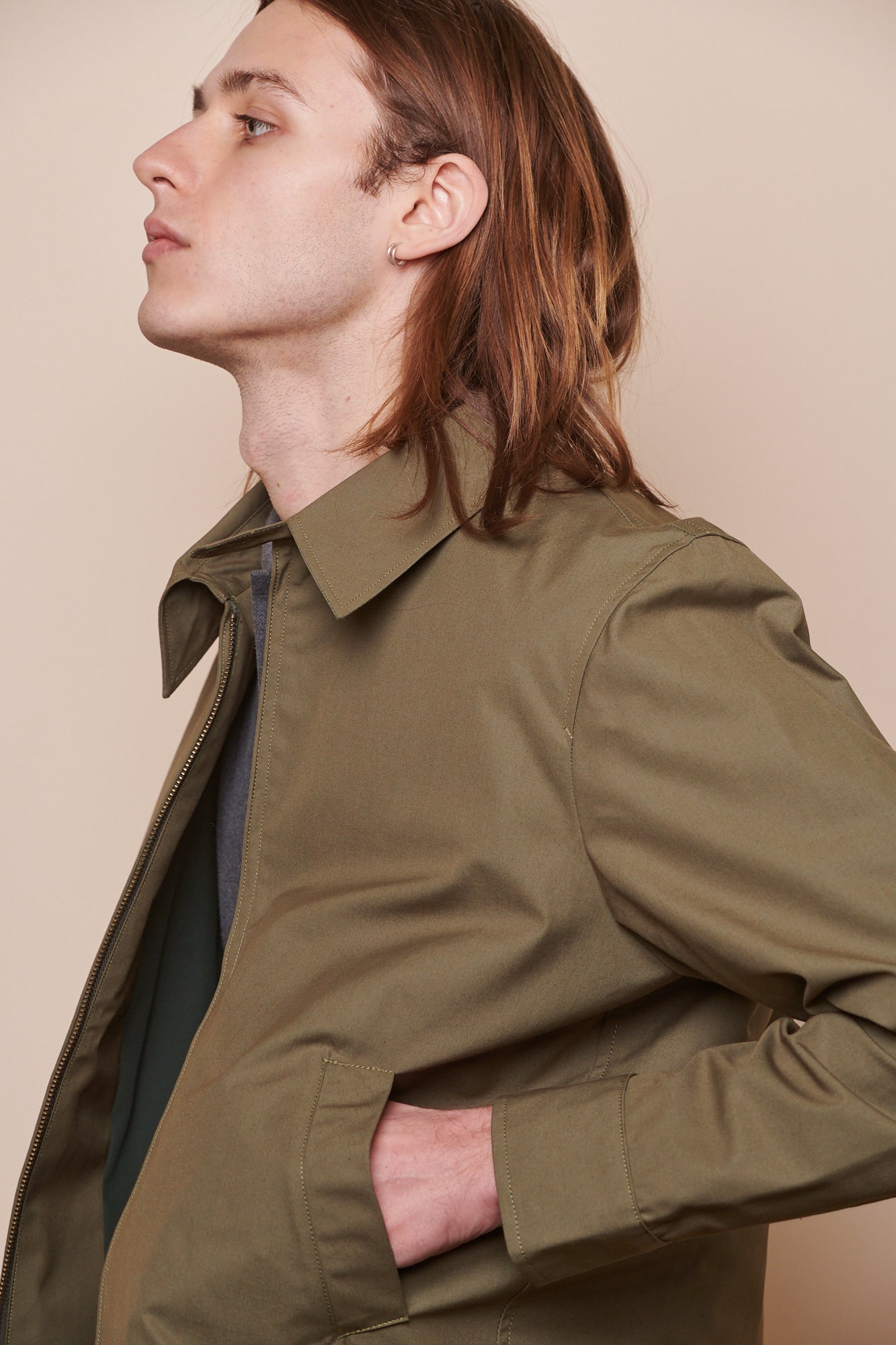 Hip up image of the side of male with hand in the pocket of collared Harrington jacket in olive