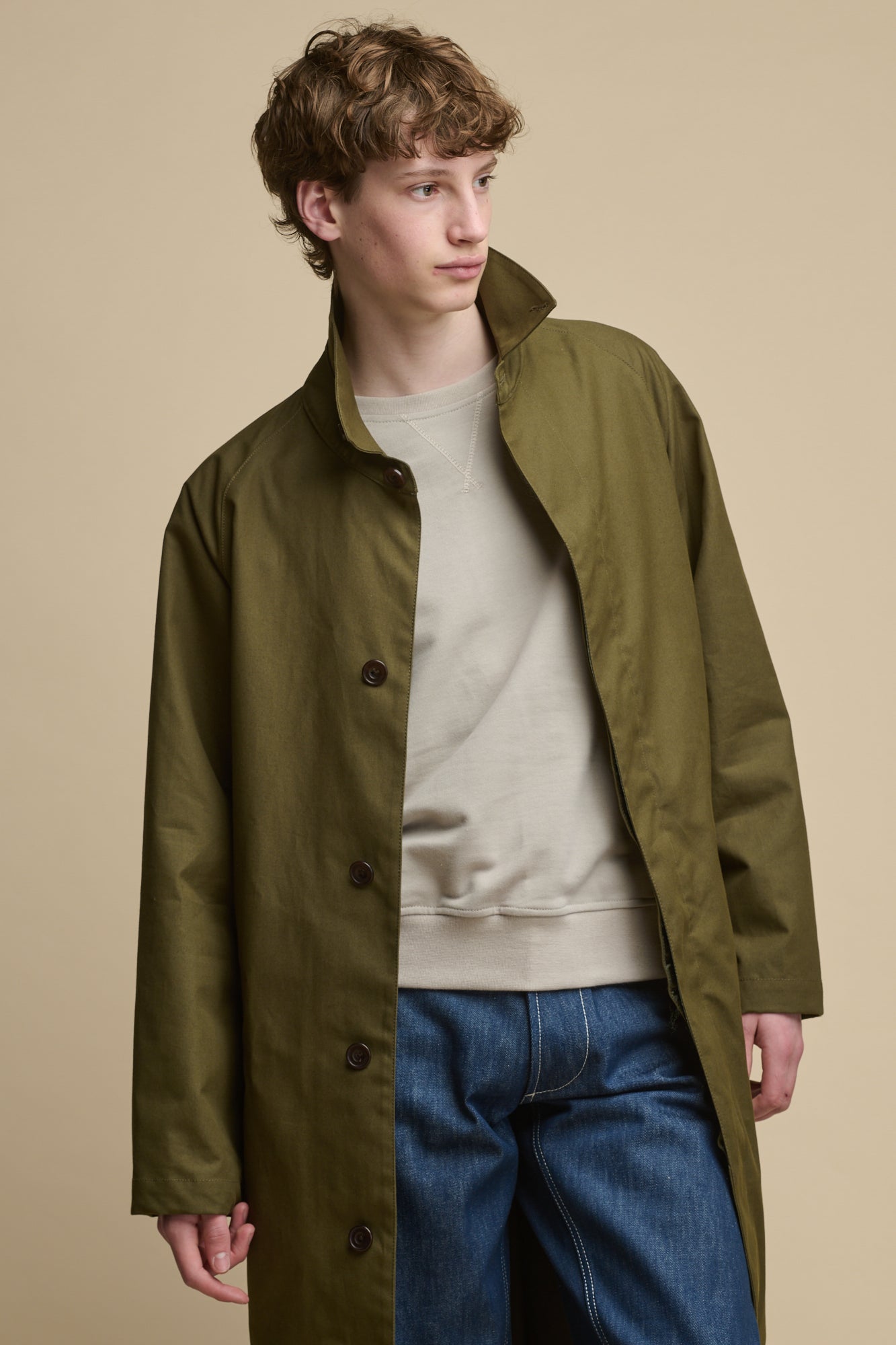 Thigh up image of the Men's Frank Raglan Belted Raincoat worn over raglan sweatshirt stone