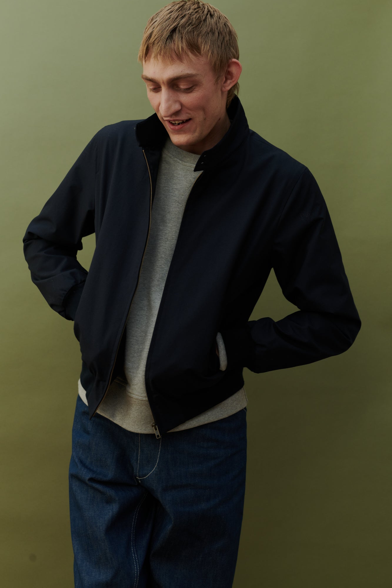 Blonde, white male wearing men's Harrington jacket in navy worn over grey raglan sweatshirt
