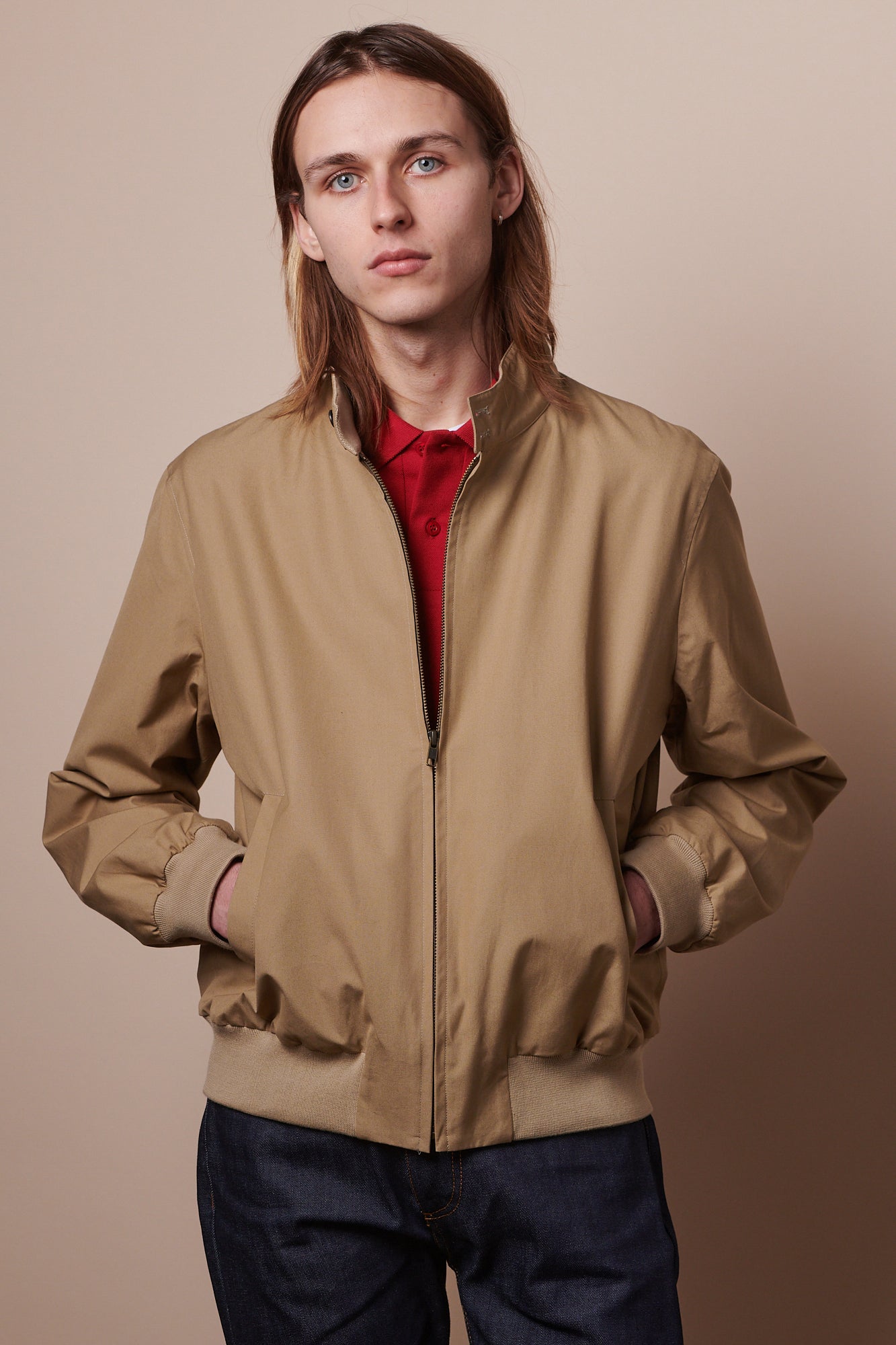 Thigh up image of male wearing Harrington jacket in stone half zipped, with hands in pockets