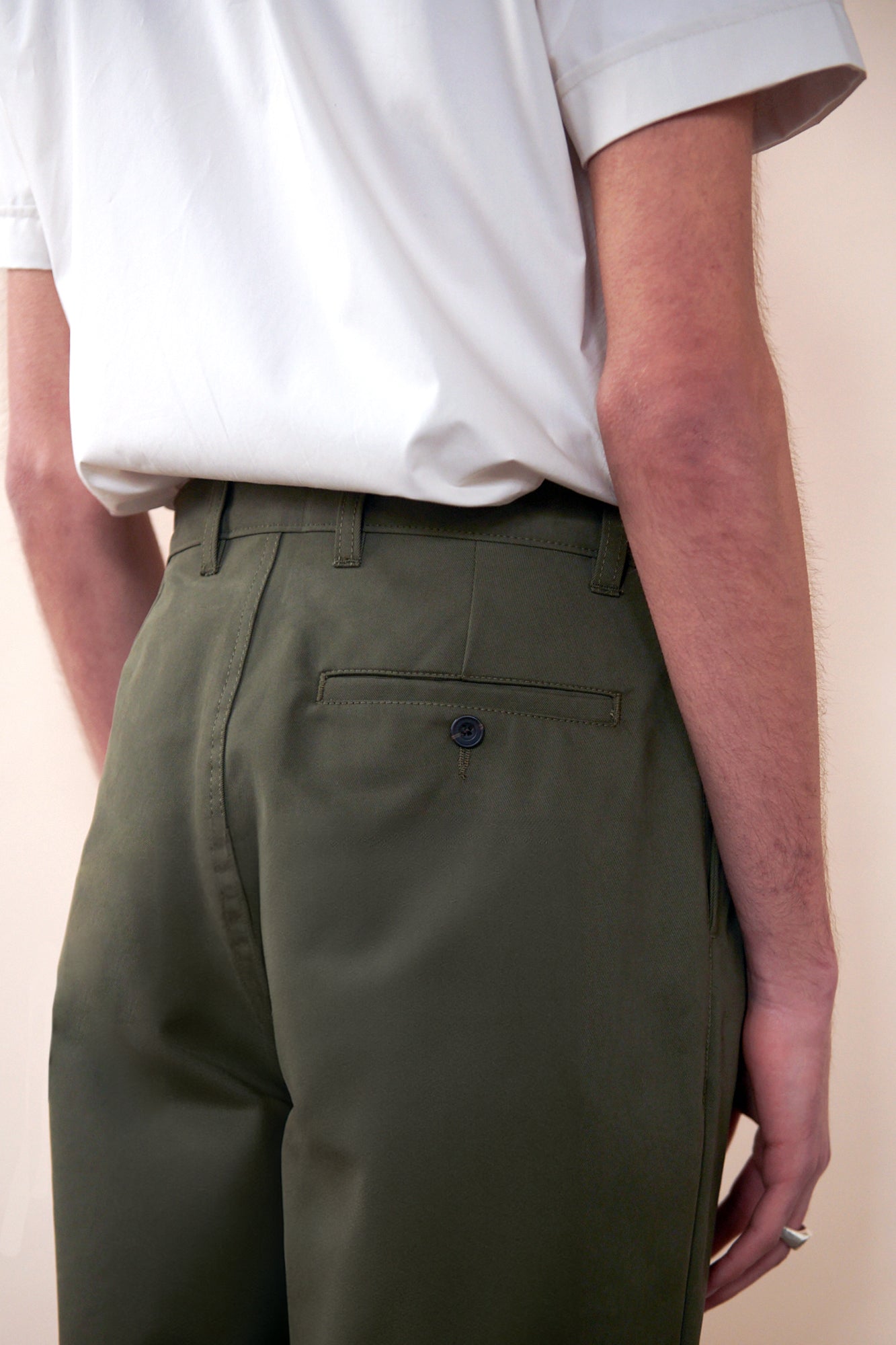 Close up of back of men's heavyweight pleated chino in olive. image shows back pocket with button and belt loops on waistband.
