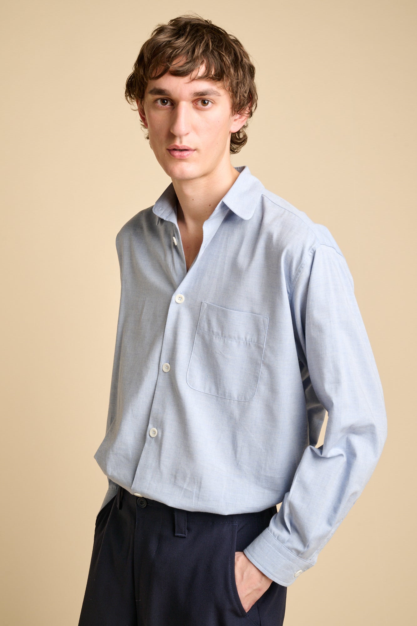 A man wearing long sleeve light blue shirt tucked into navy trousers.