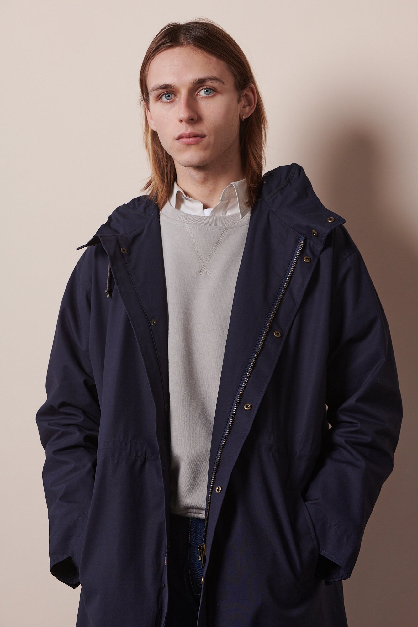 male with hands in pockets of unzipped parka in navy, shirt and raglan sweatshirt layered underneath