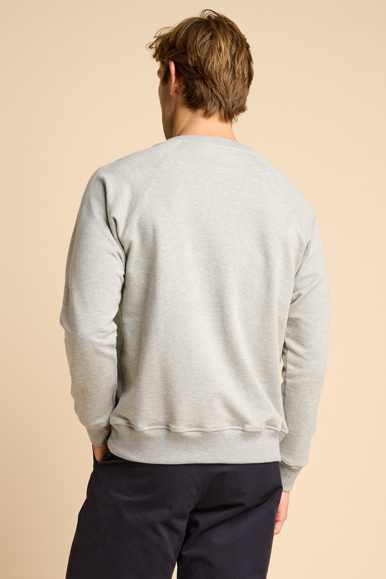 Man wearing a grey sweatshirt and dark pants on a beige background.