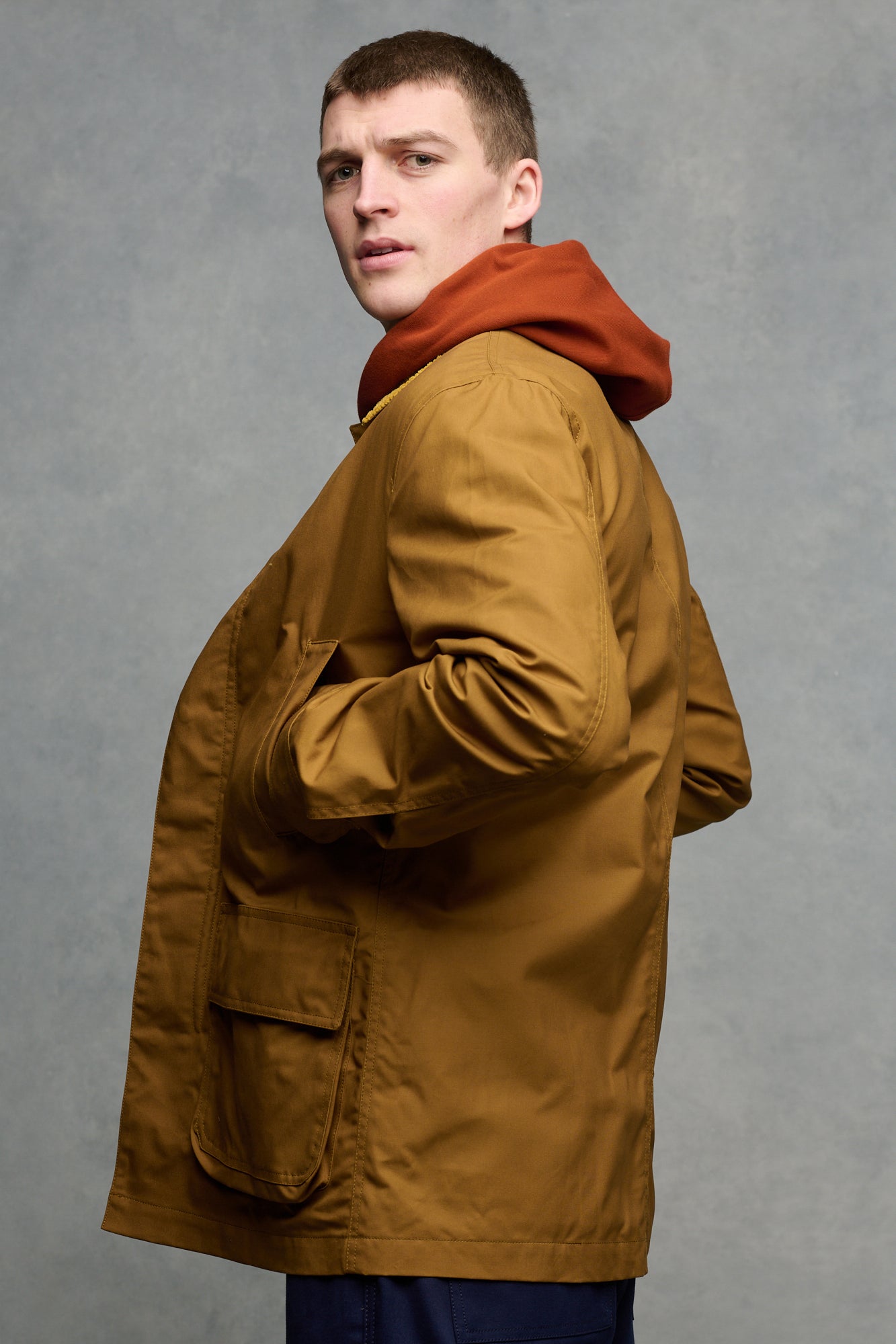 The side of brunet male wearing barn jacket in dark tan with hand in front pockets.