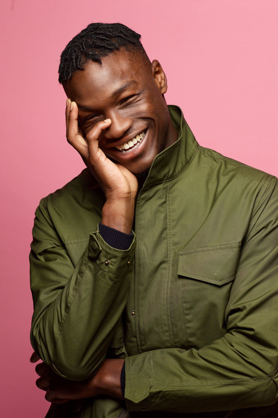 young black male smiling as he is wearing an olive field jacket from community clothing