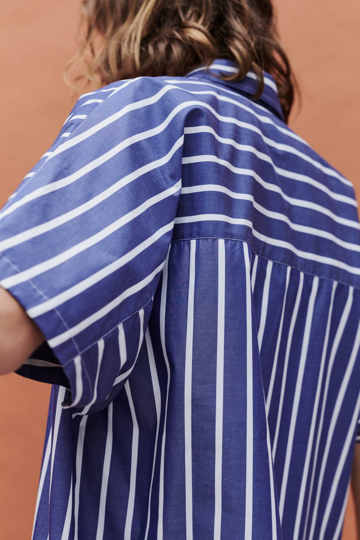back of female wearing Ava short sleeve shirt in front of a coral background
