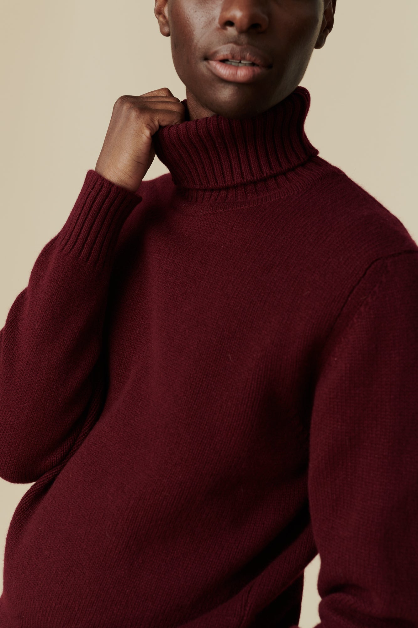 Male wearing lambswool roll neck in burgundy. Detail image of ribbed roll neck and cuff.