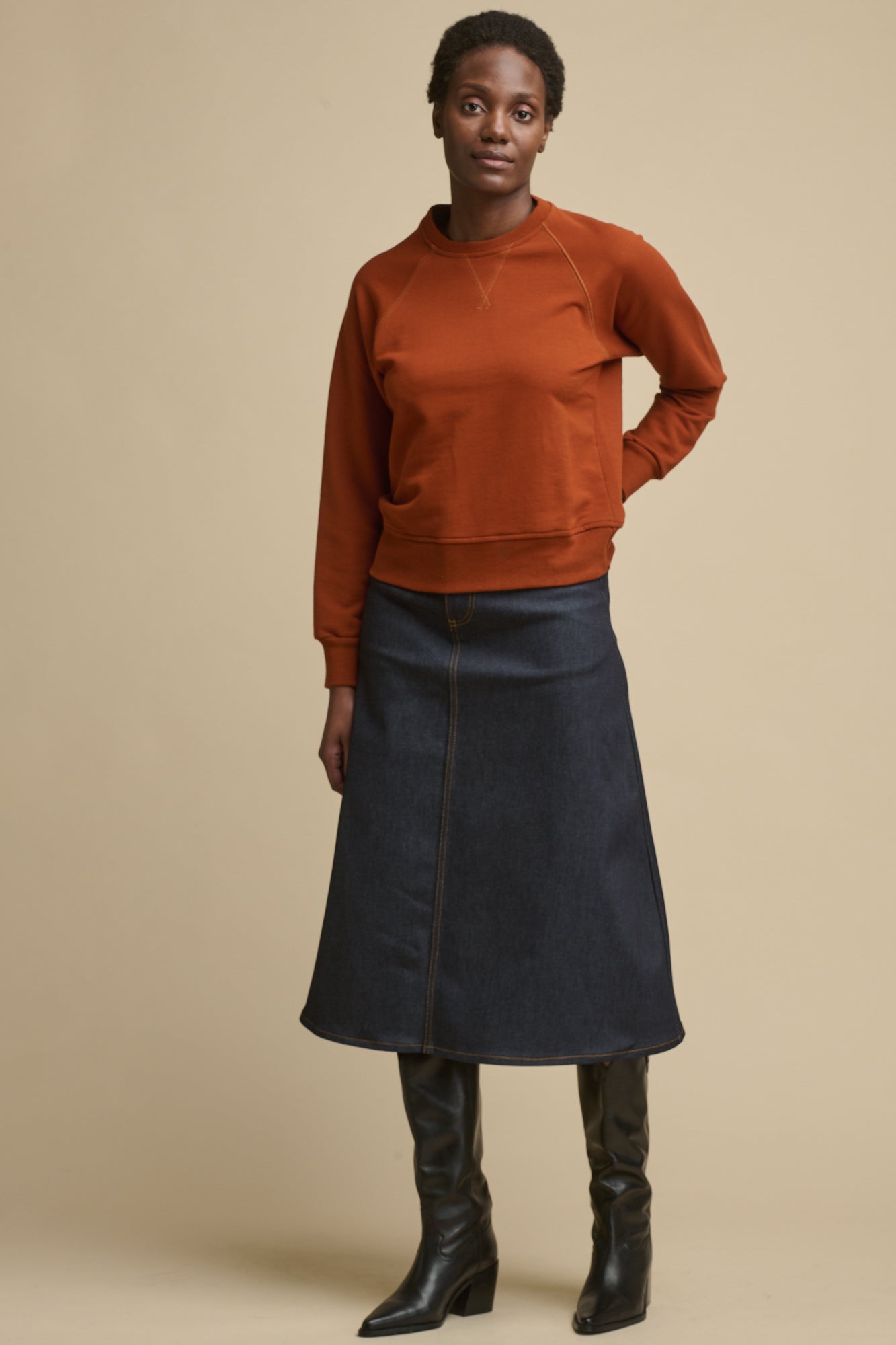 Full body image of the front of black female wearing Bobbie a line denim skirt in indigo paired with cinnamon raglan sweatshirt