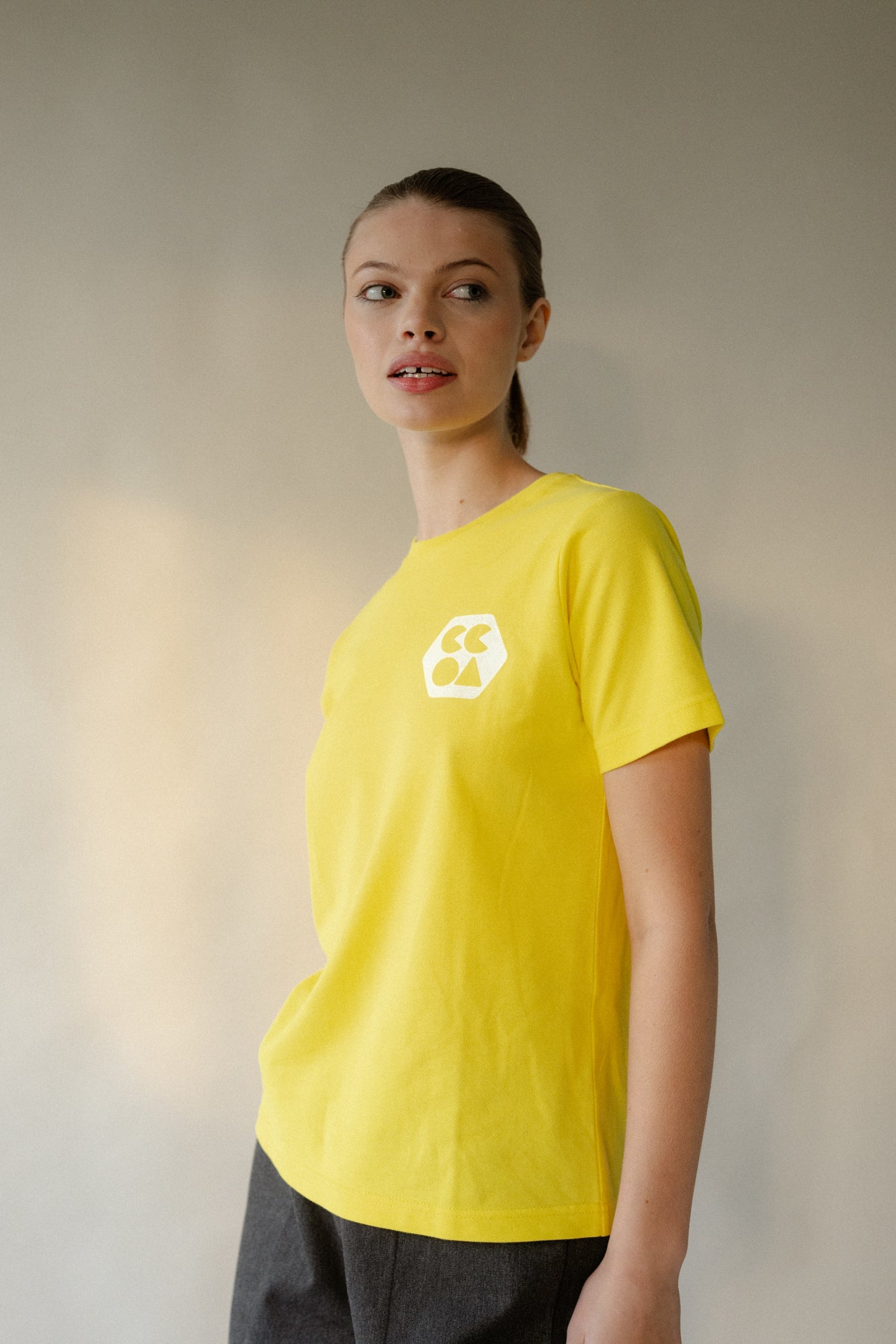 Thigh up image of female wearing women's breathable short sleeve t shirt plastic free in canary yellow with white CCOA logo