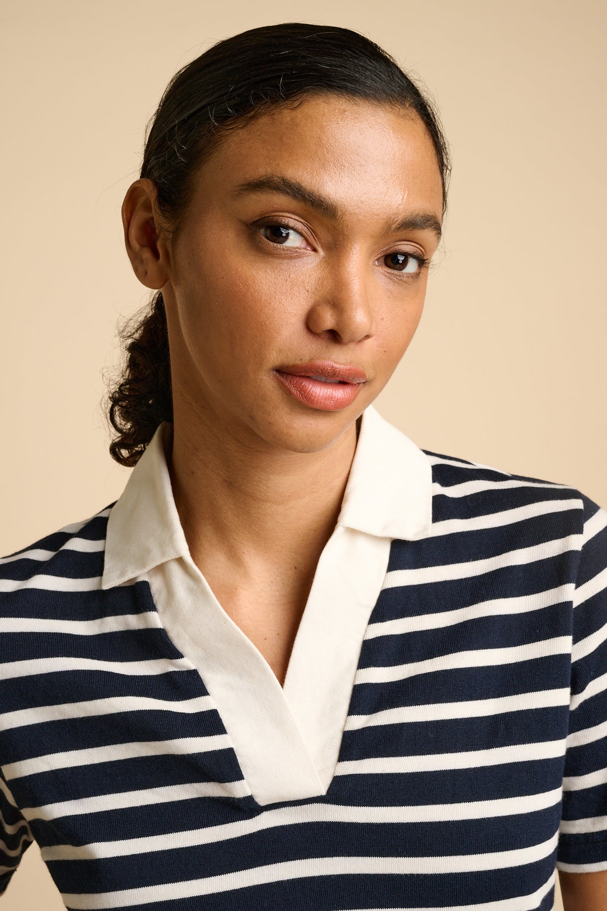 Woman wearing a navy and ecru striped top with collar against a beige background.