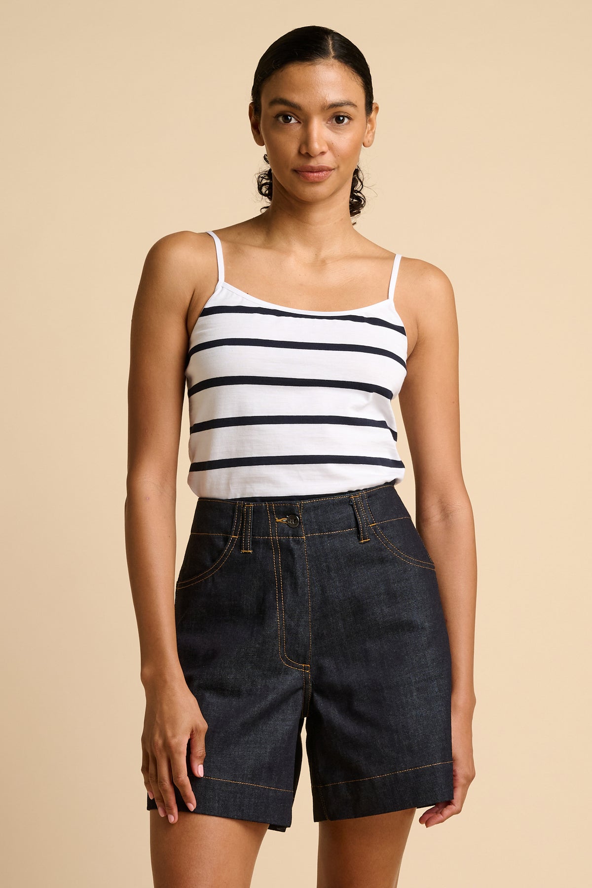 Woman wearing a striped camisole and denim shorts on a beige background