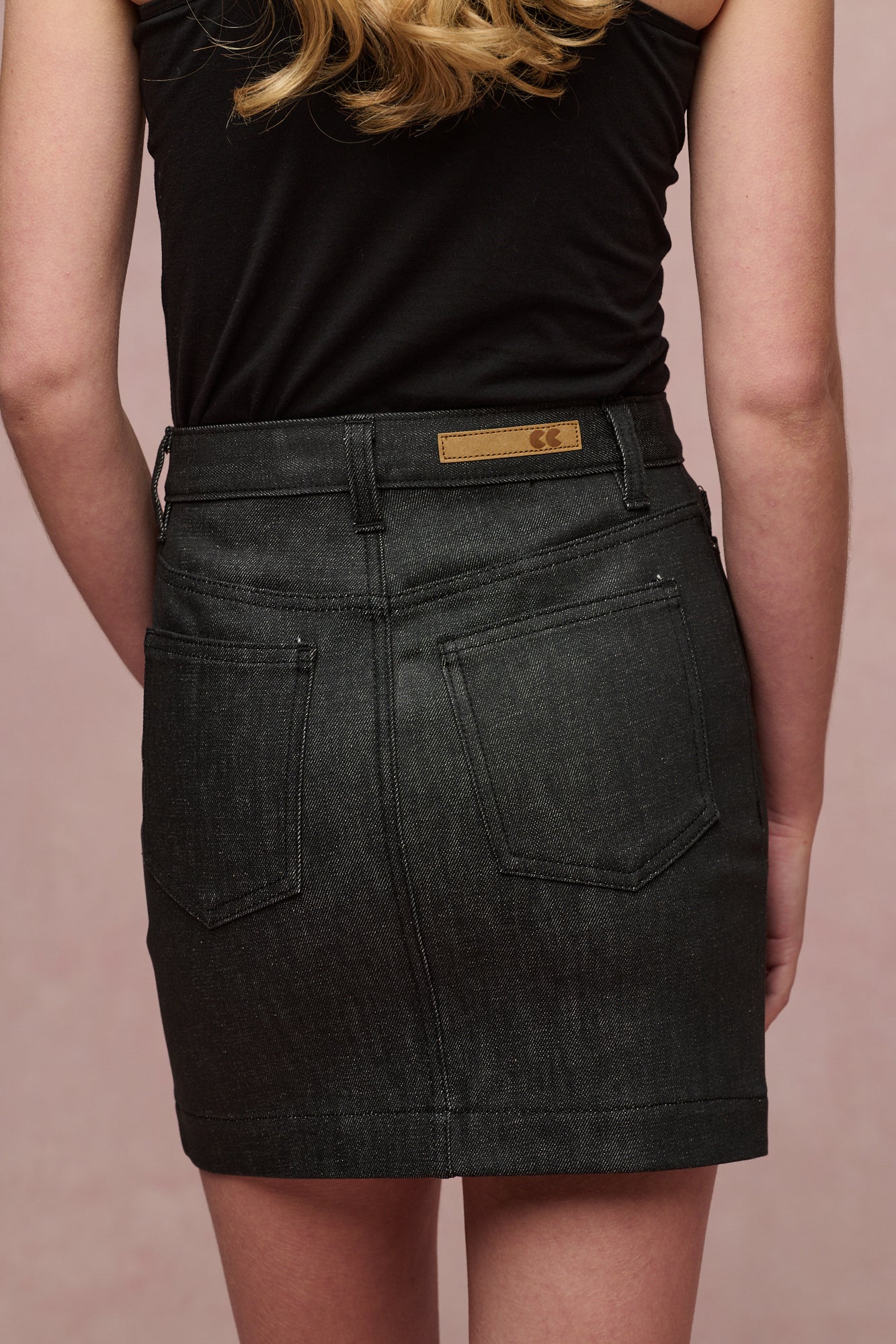 Image showing a close up of the back of Charlie denim mini skirt in black. Two back pockets, belt loops and CC logo jean patch on the waistband