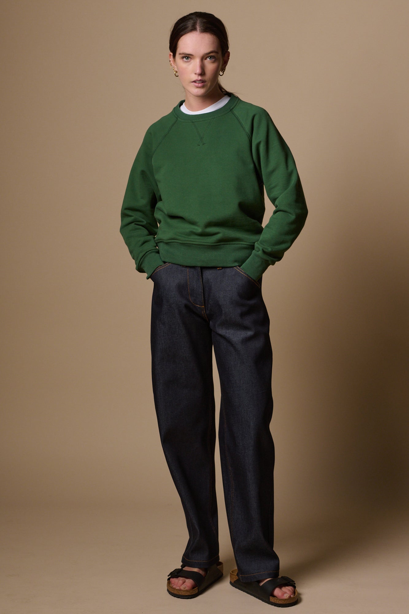 Full body image of female with hands in front pockets of chore jeans in indigo paired with raglan in bottle green