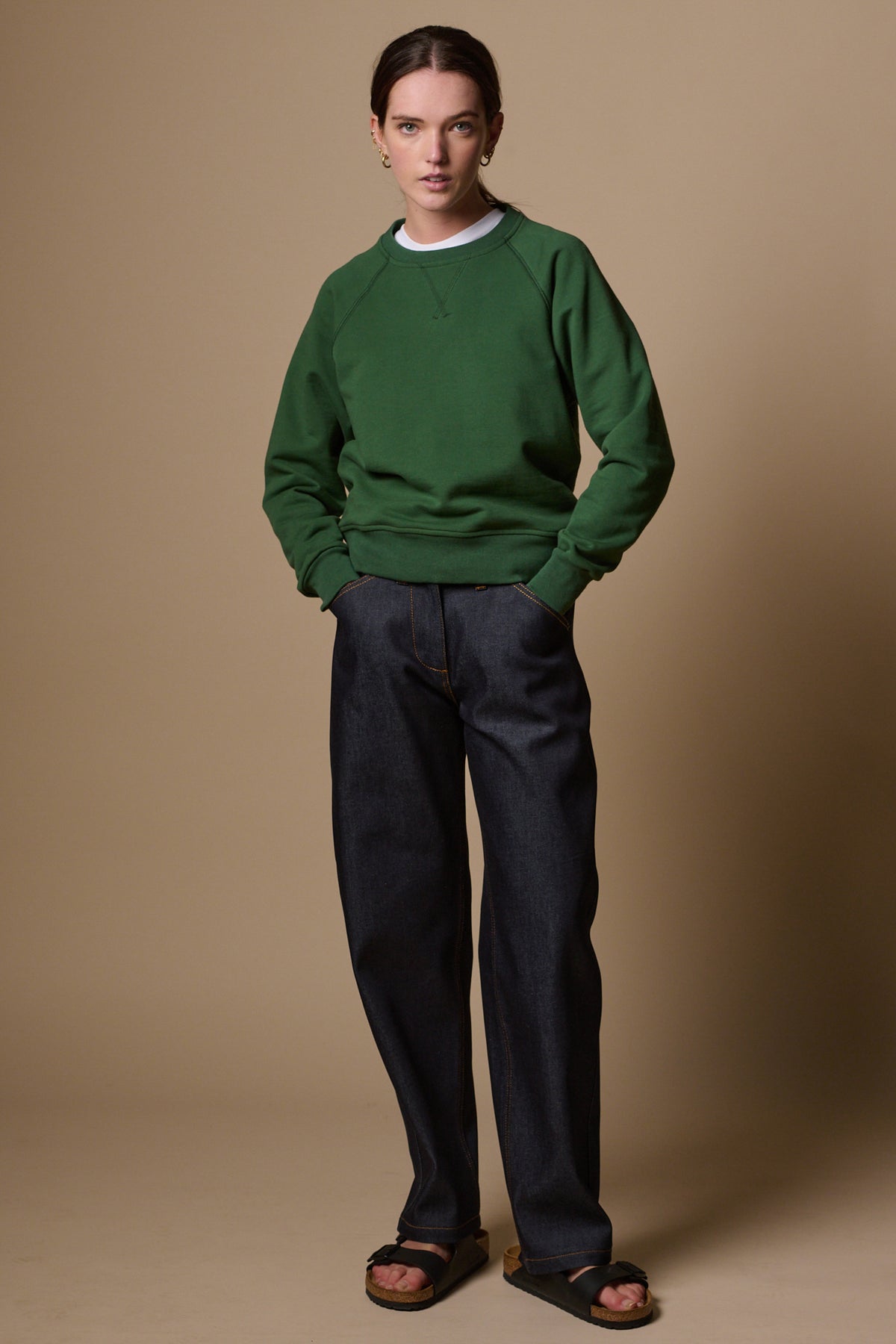 Full body image of female with hands in front pockets of chore jeans in indigo paired with raglan in bottle green