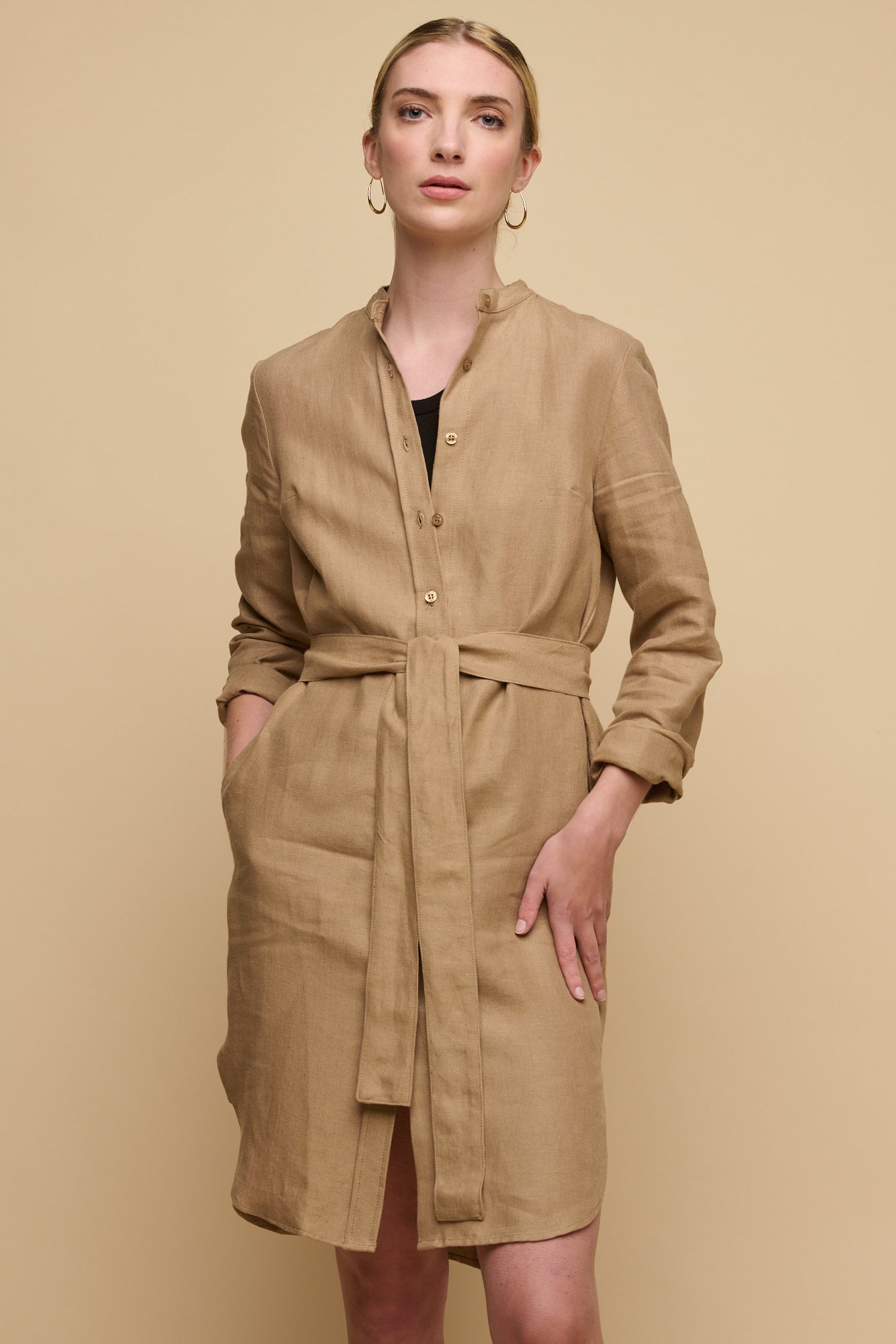 Knee up image of female wearing collarless shirt dress in truffle linen worn over black vest