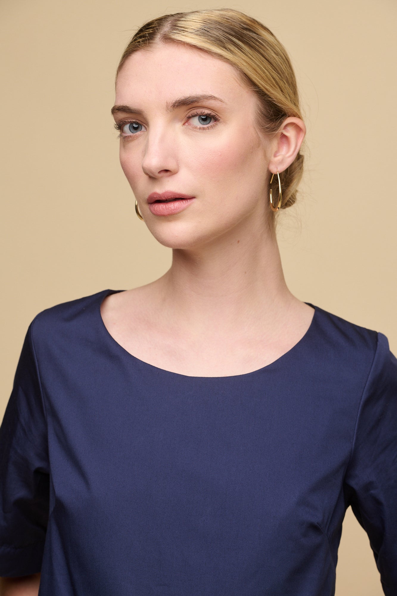 Blonde female with fair skin wearing crew neck gathered dress in navy, with a hand in one of the front pockets