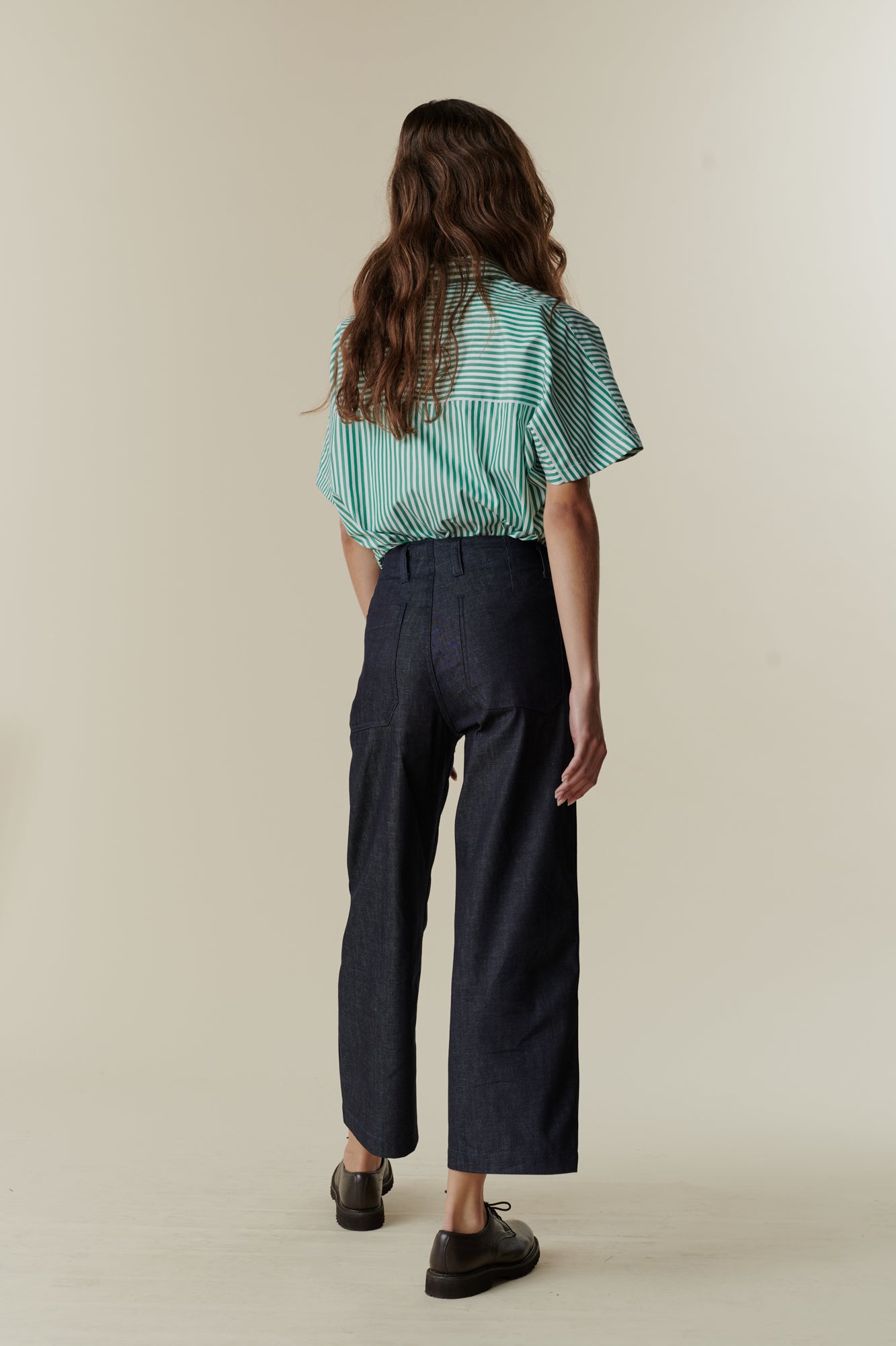 Full body back image of female wearing cropped work trousers in denim 