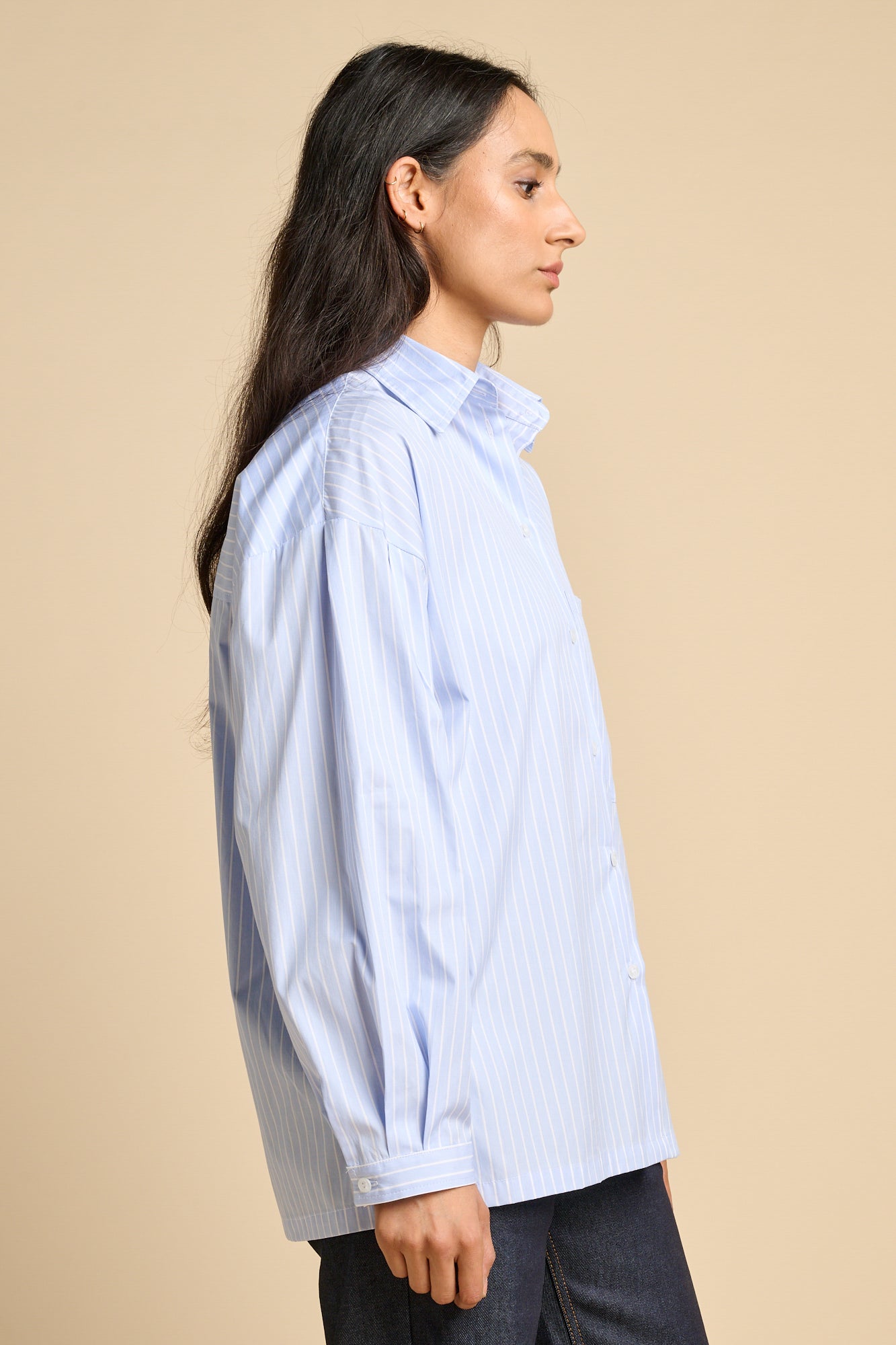 Side profile of a woman wearing long sleeve Esme shirt in pale blue and white stripe.