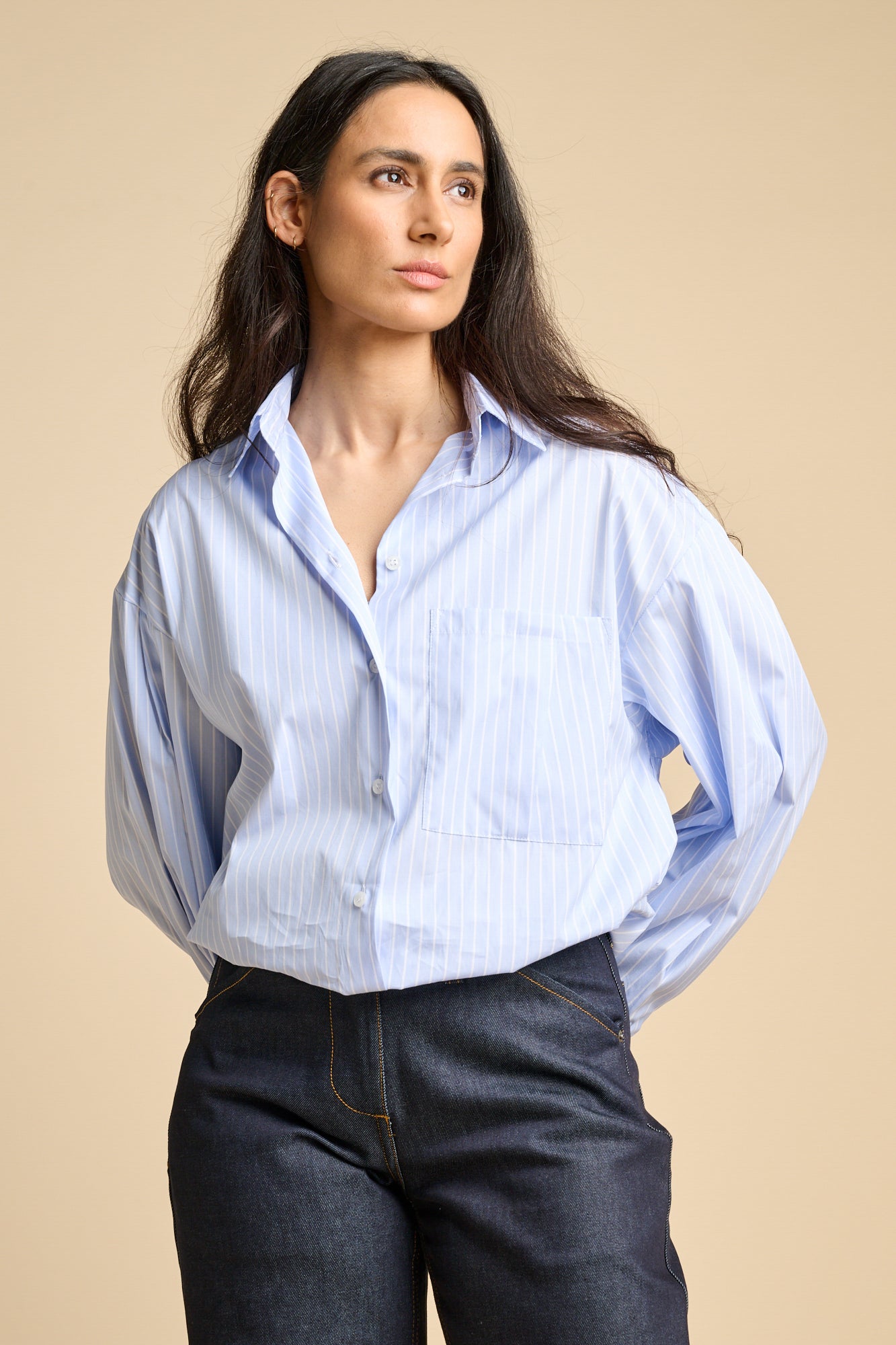 A woman wearing long sleeve blue and white stripe Esme shirt tucked into indigo jeans.