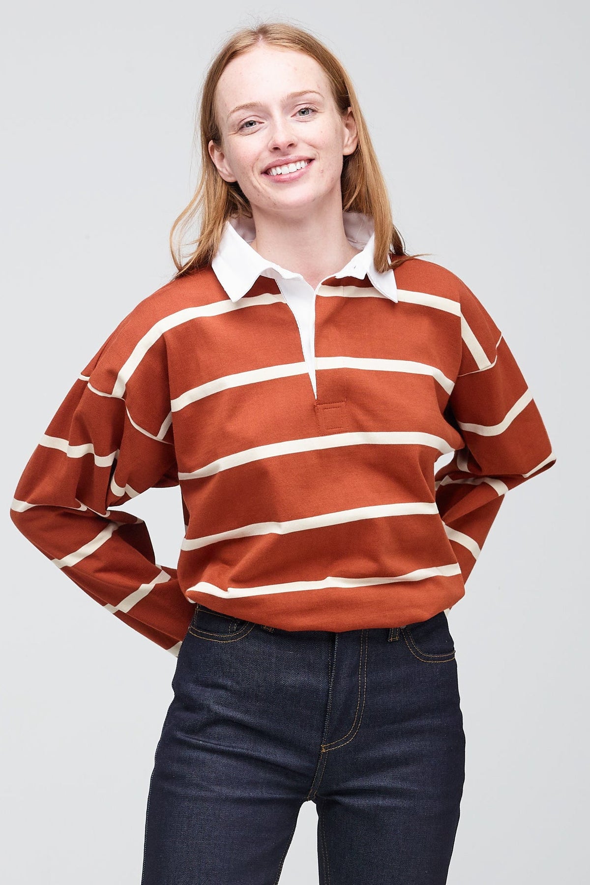 Ginger, white female wearing fine stripe rugby shirt in cinnamon and ecru tucked into jean 