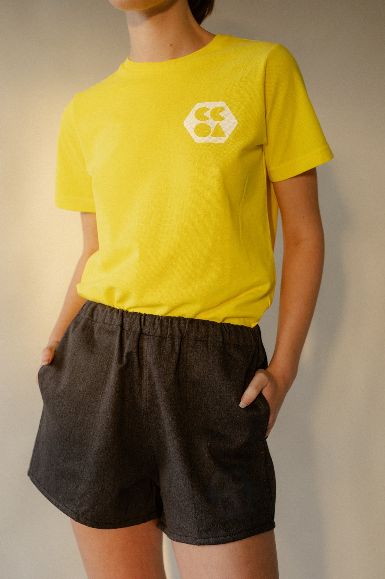 Female wearing women's heavyweight sports short plastic free in charcoal marl with CCOA logo and her hands in front pockets.