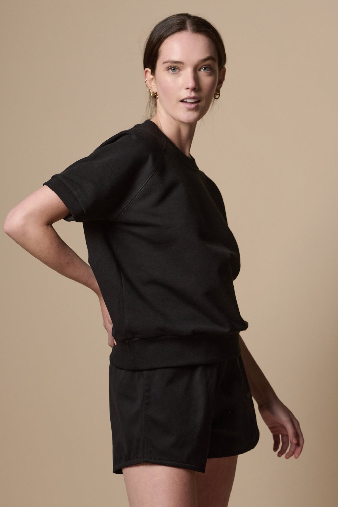 Side of female wearing heavyweight sports short plastic free in black with CCOA logo on models left leg paired with short sleeve raglan training top in black