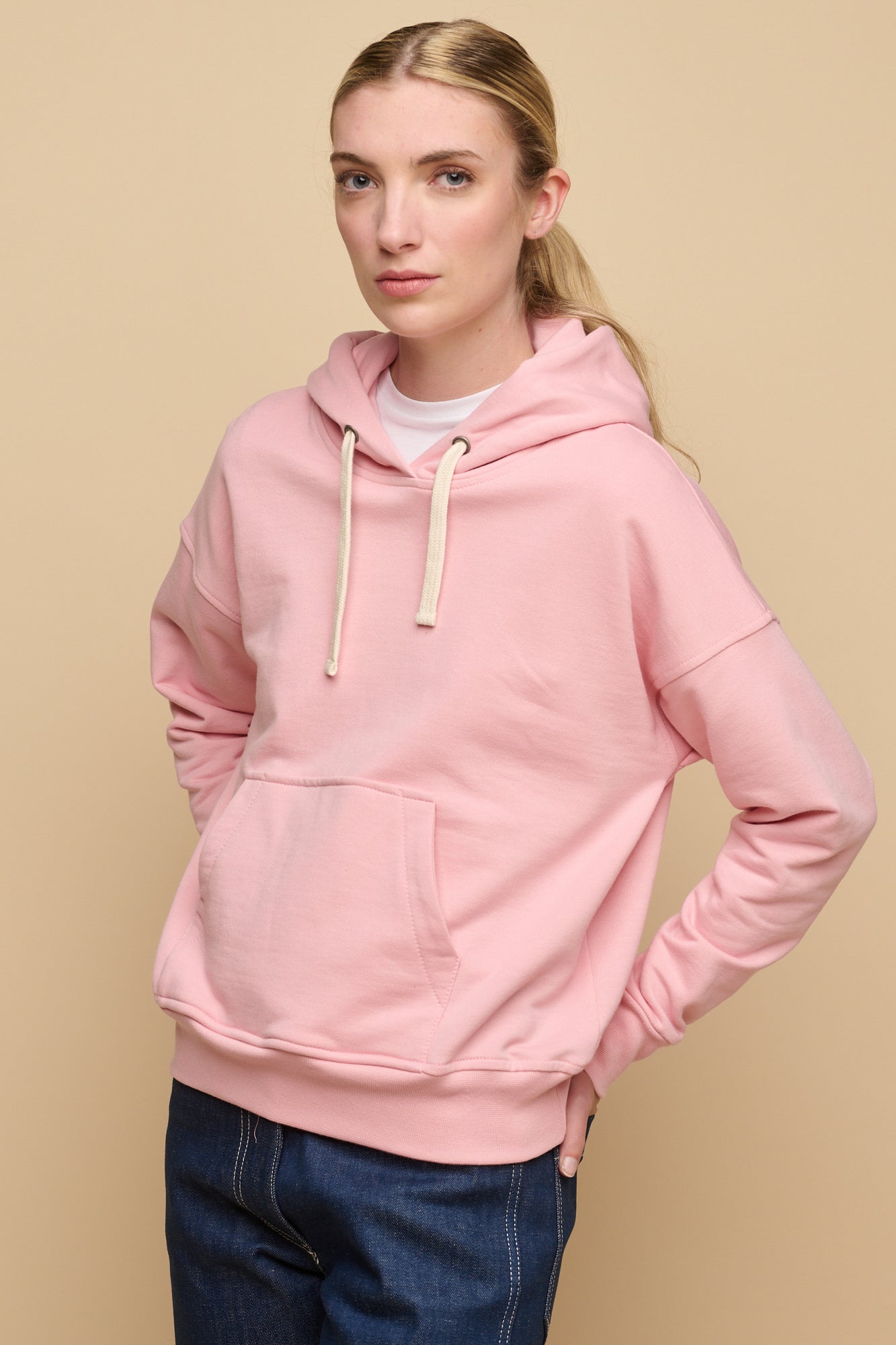 Thigh up image of the back of female wearing pale pink hooded sweatshirt paired with work jeans in blue