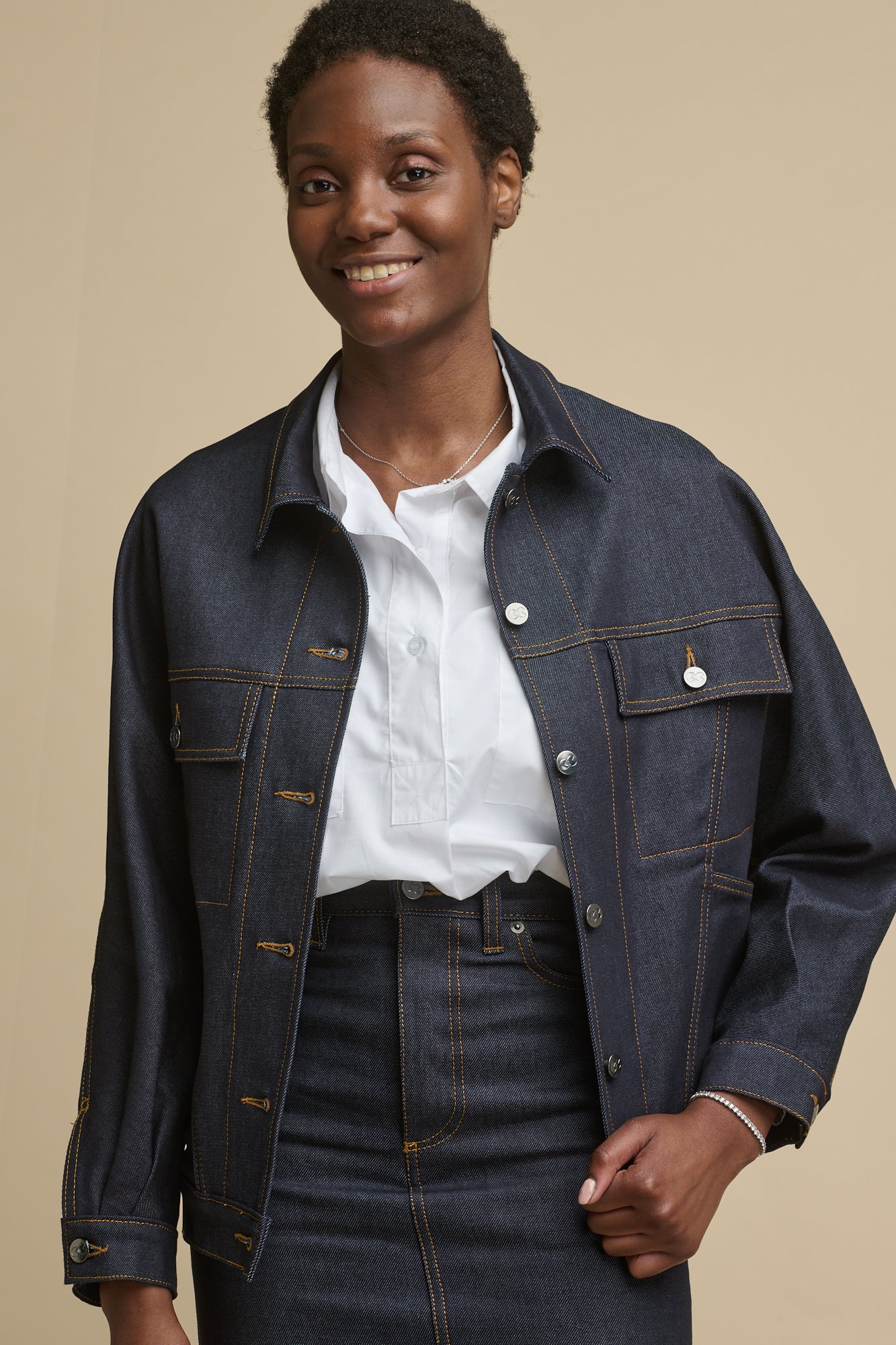 Thigh up image of smiley female wearing Jodie denim jacket in indigo with two front chest pockets with flats 