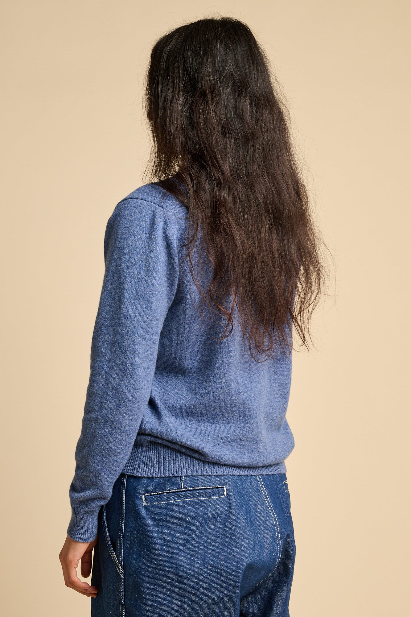 The back of a woman wearing lambswool crew neck jumper in denim marl paired with blue jeans.