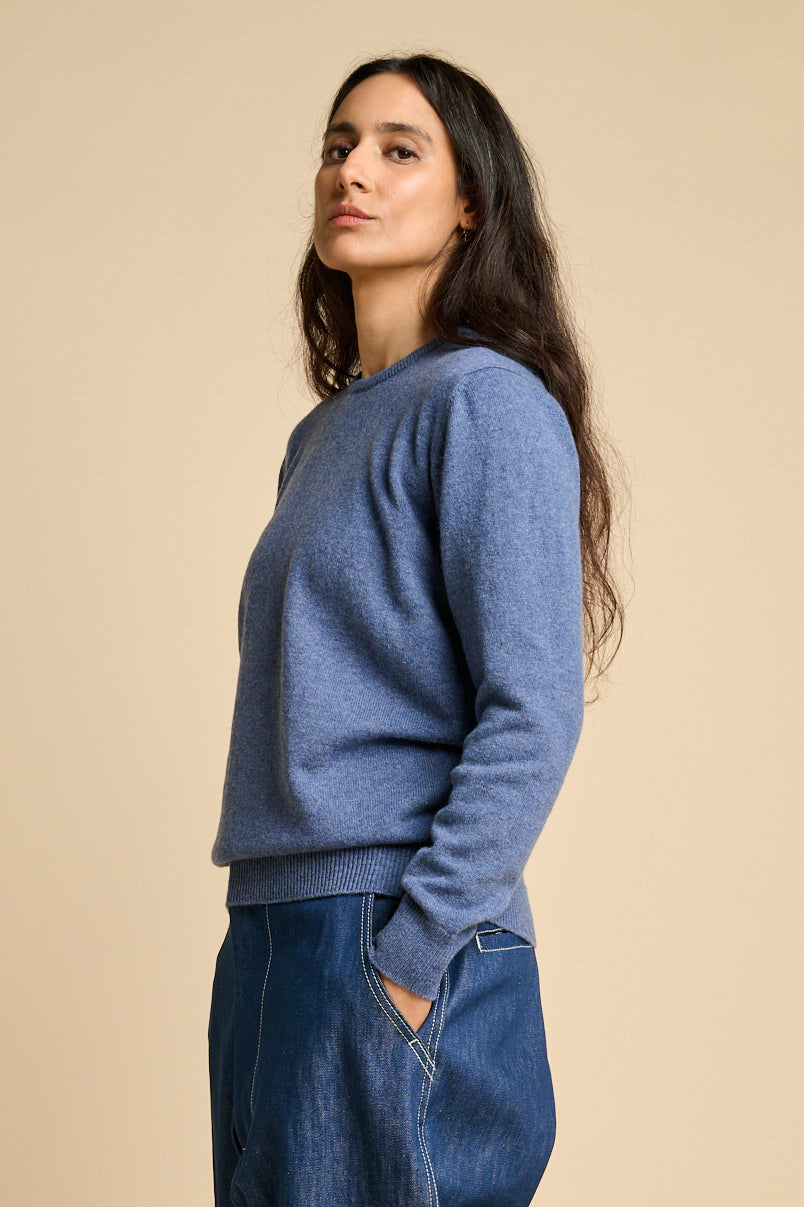 A woman wearing lambswool crew neck jumper in denim marl paired with blue jeans.