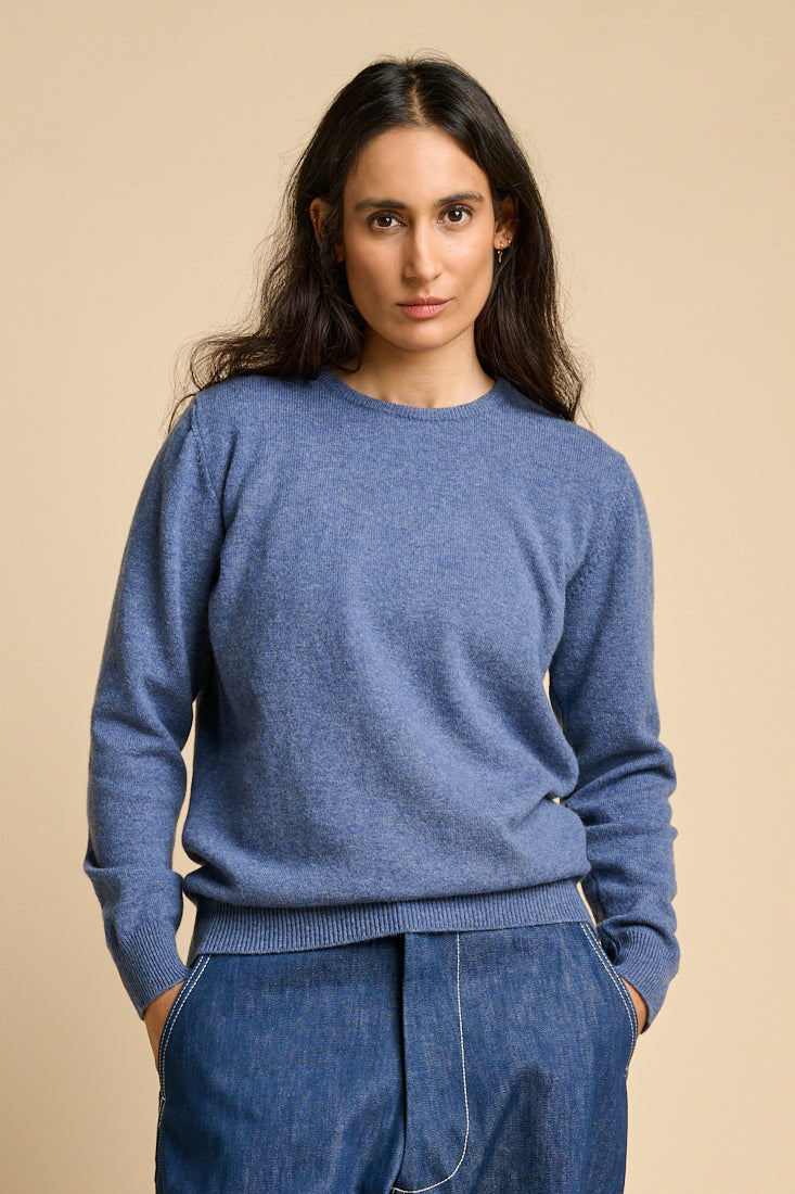 A woman wearing lambswool crew neck jumper in denim marl paired with blue jeans.