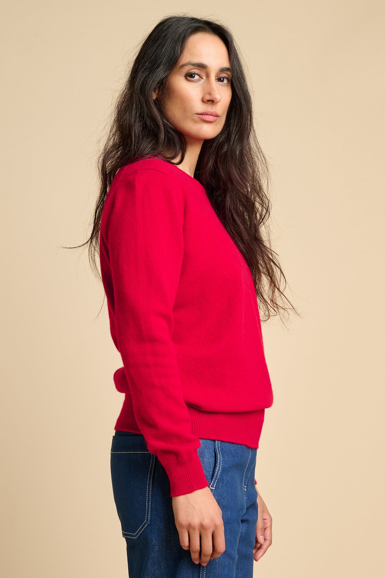 The side of woman wearing lambswool crew neck jumper in red paired with blue. 