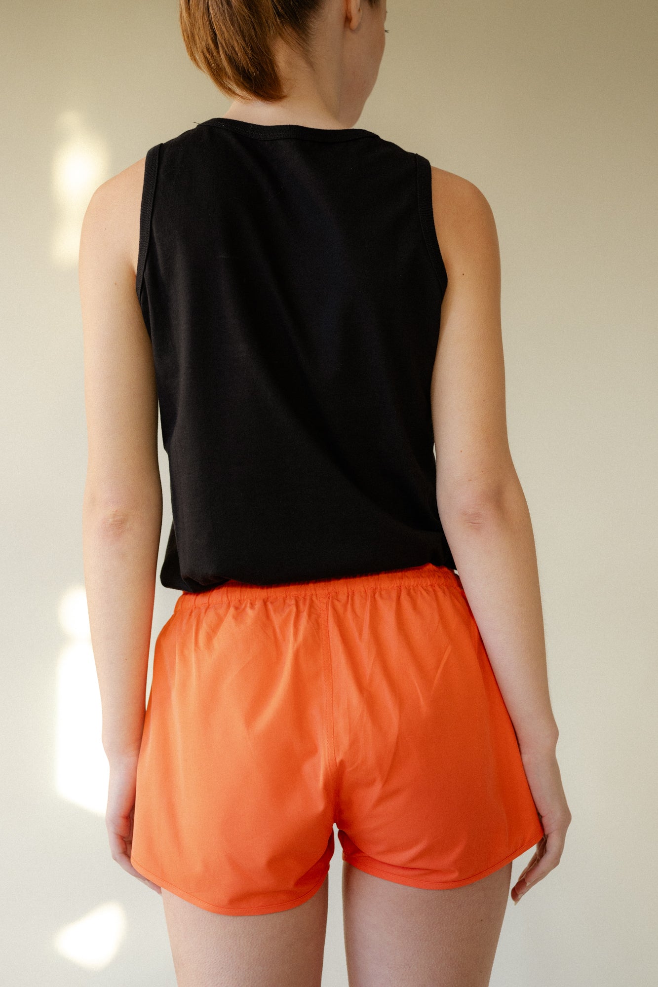 shot of female back of head to thigh wearing lightweight running shorts plastic free flame red.