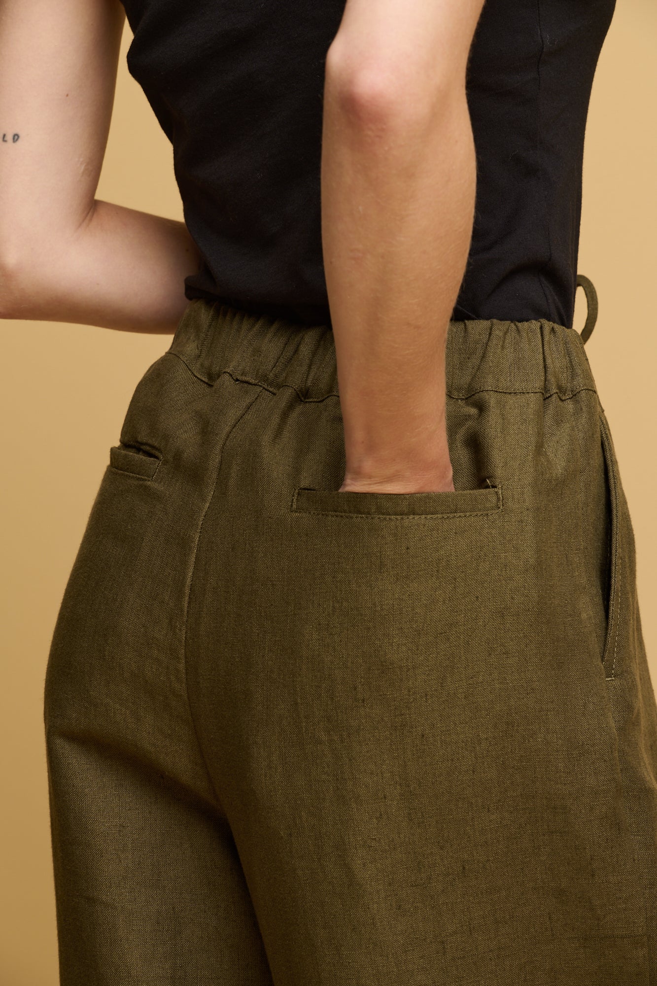 Close up of the back of linen trousers with females hand in one of the back jet pockets.