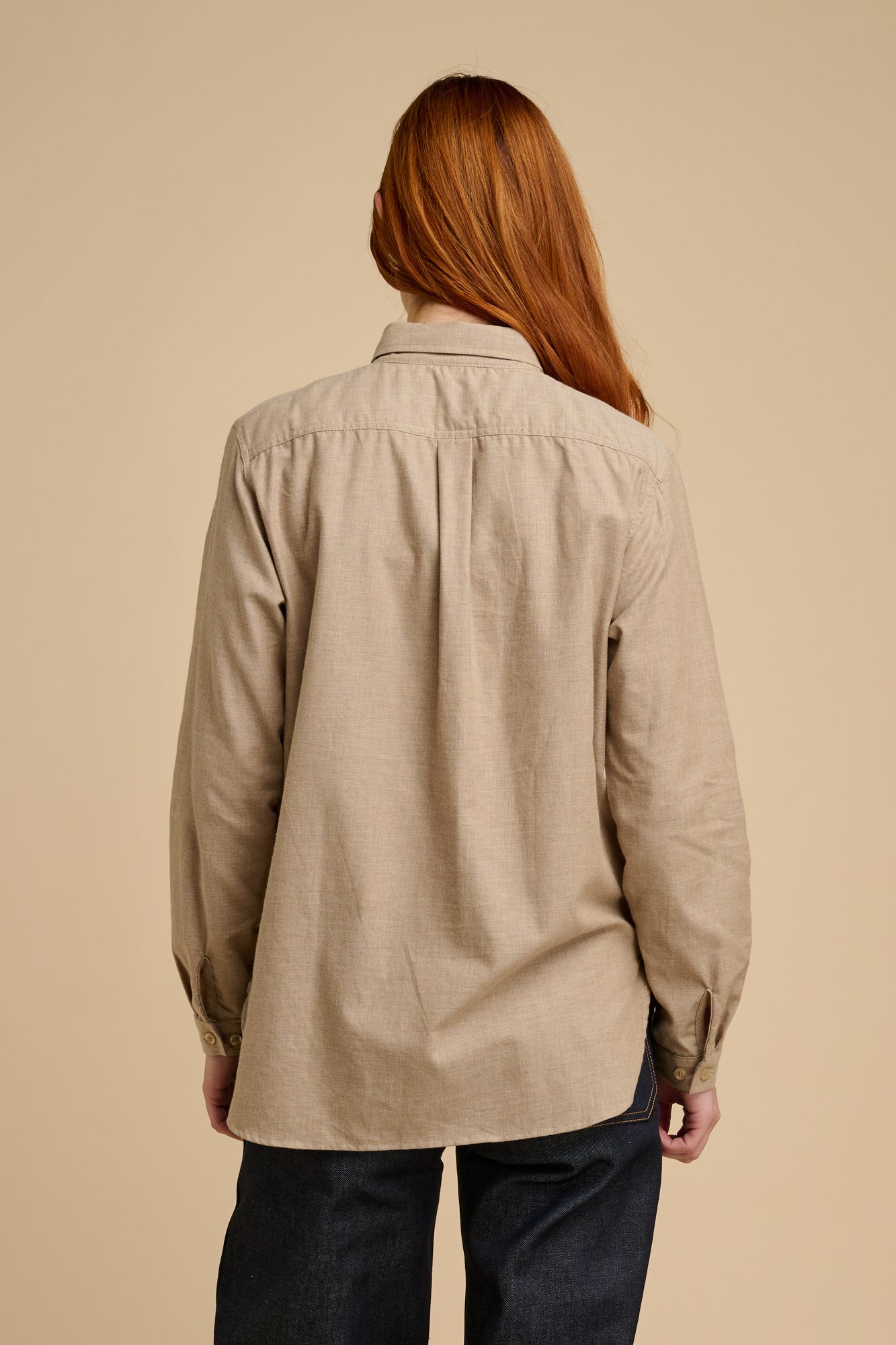 The back of woman wearing beige shirt against a beige background
