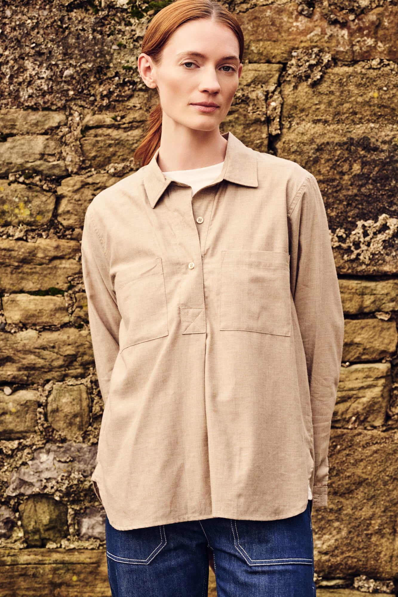 Woman wearing a beige shirt standing against a stone wall