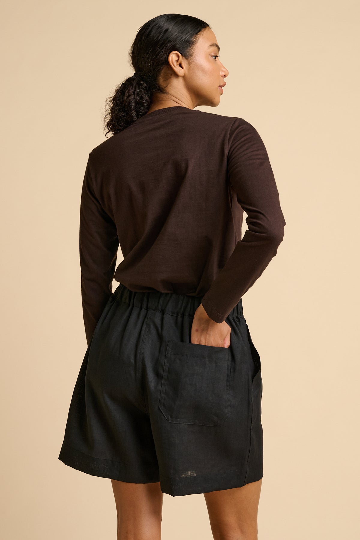Woman wearing a brown long-sleeve top and black shorts on a beige background.
