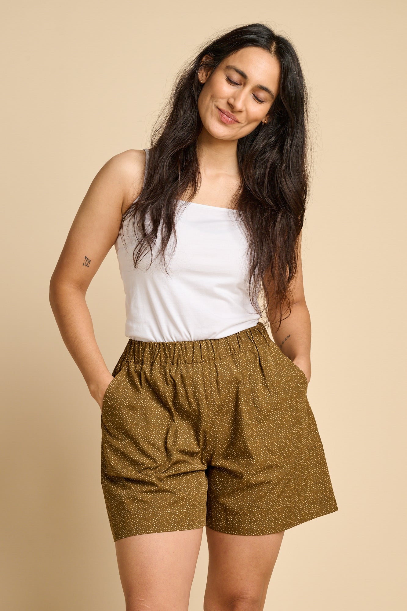 A woman wearing white cami and brown polka dot pull up shorts. 