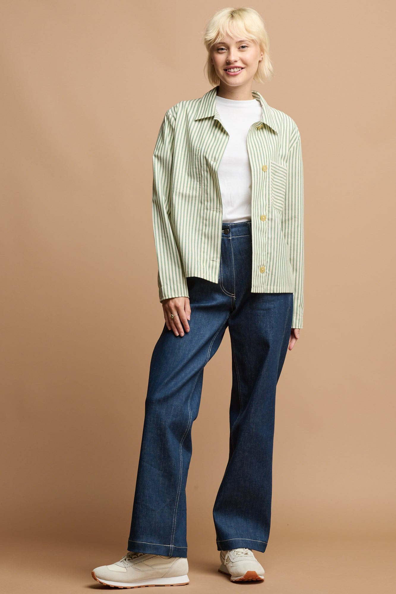 Blonde female wearing green and white stripe elena shirt open over white t shirt, paired with blue Community Clothing work jeans
